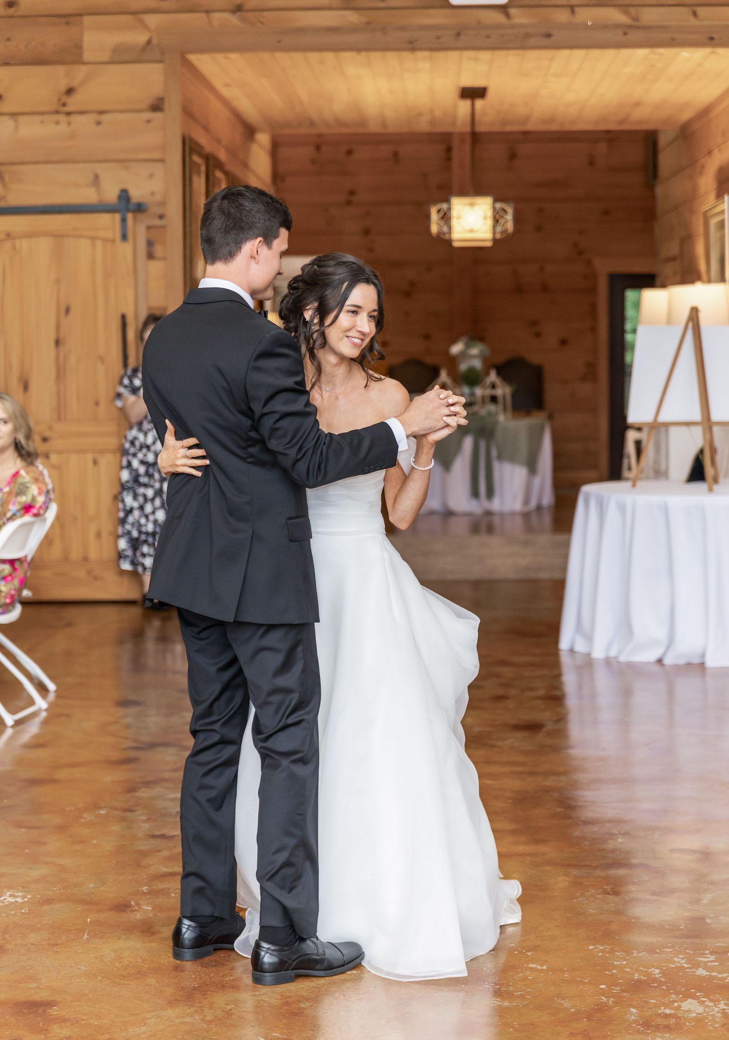 Dancing couple in formal attire share an intimate moment in a wooden reception hall.