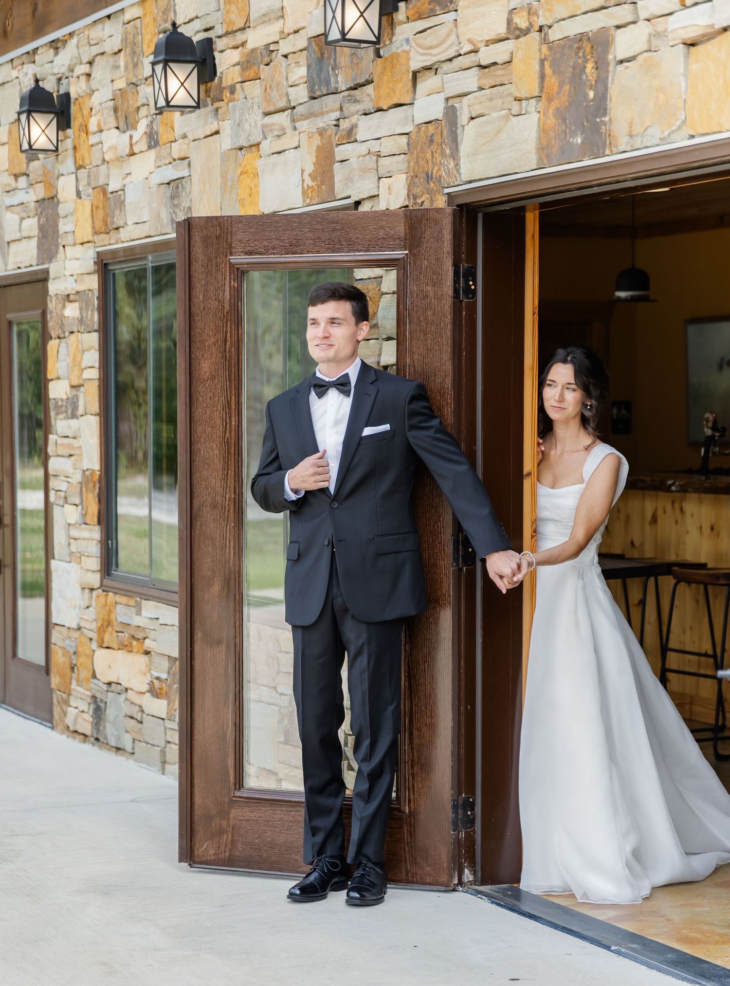 Bride and groom share joyful reactions while peeking around doorways during wedding photo session.