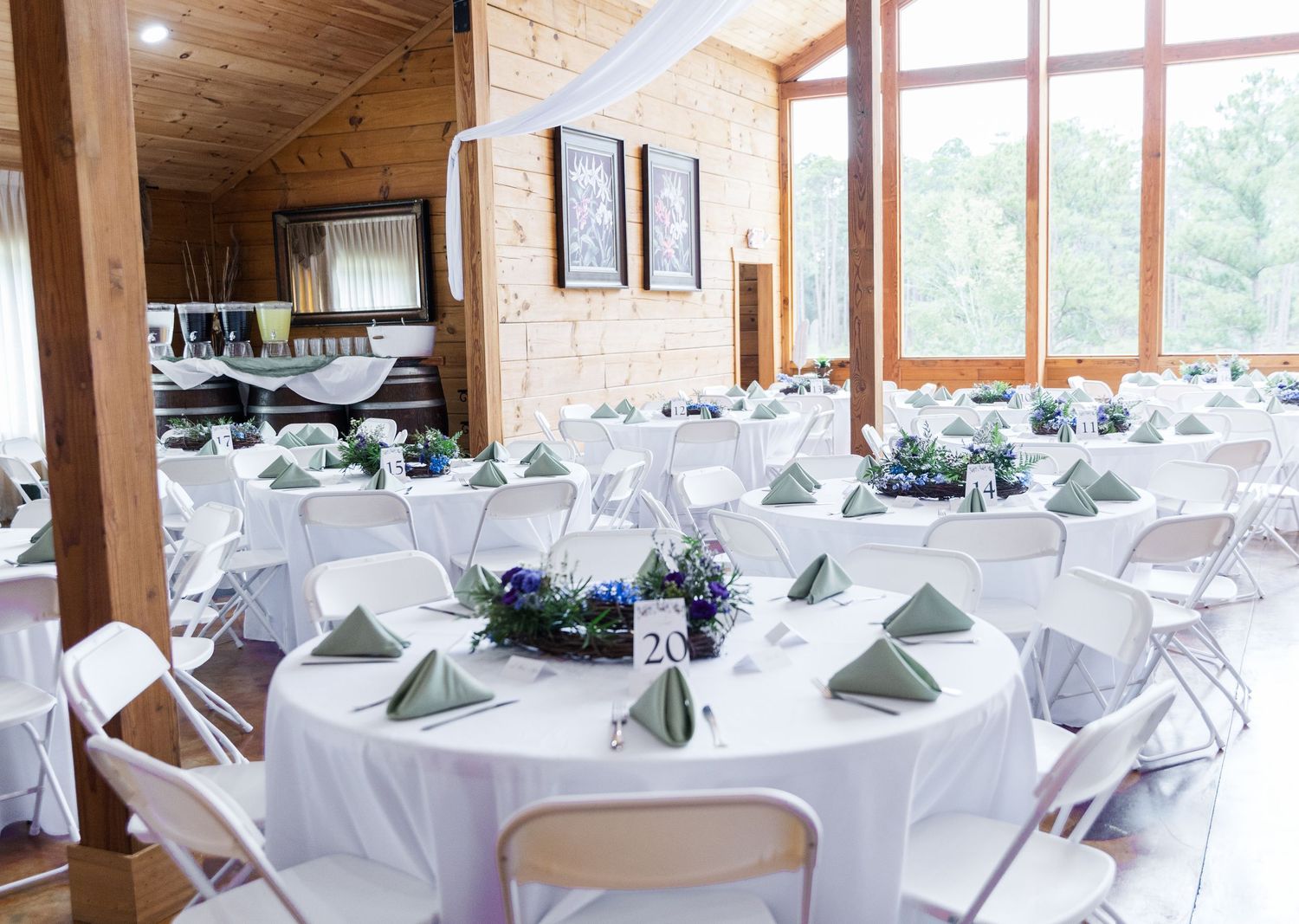 A panoramic view of an elegant wedding reception venue with white-clothed round tables and wooden beam ceiling details.