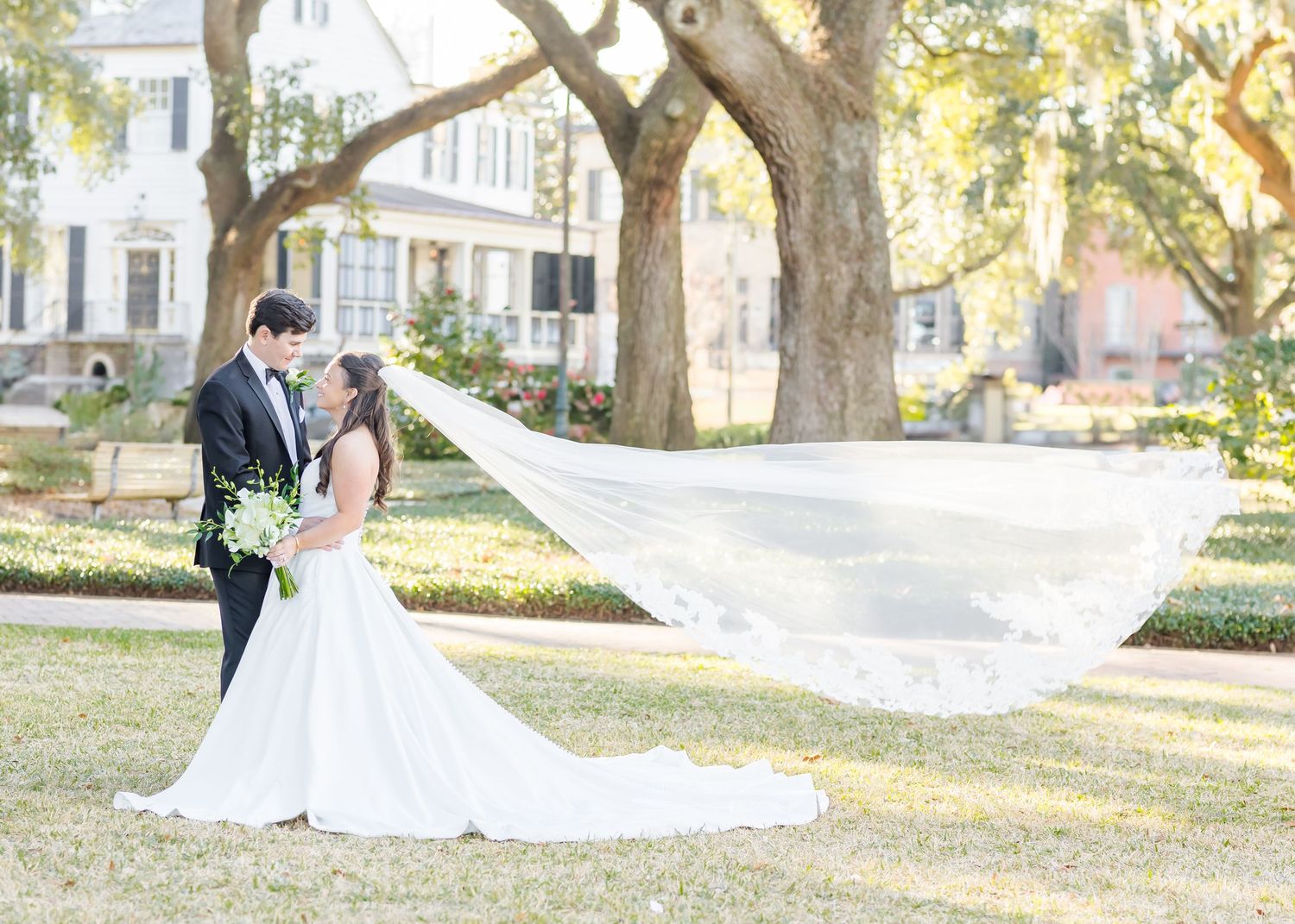 A flowing wedding veil catches the sunlight and breeze in a romantic outdoor garden setting.
