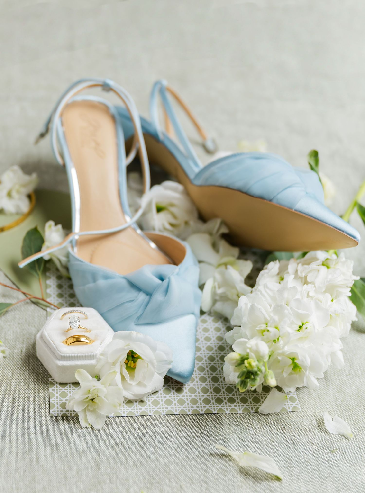 Light blue satin knotted bow heels with diamond ring in white velvet hexagon box and white floral details.
