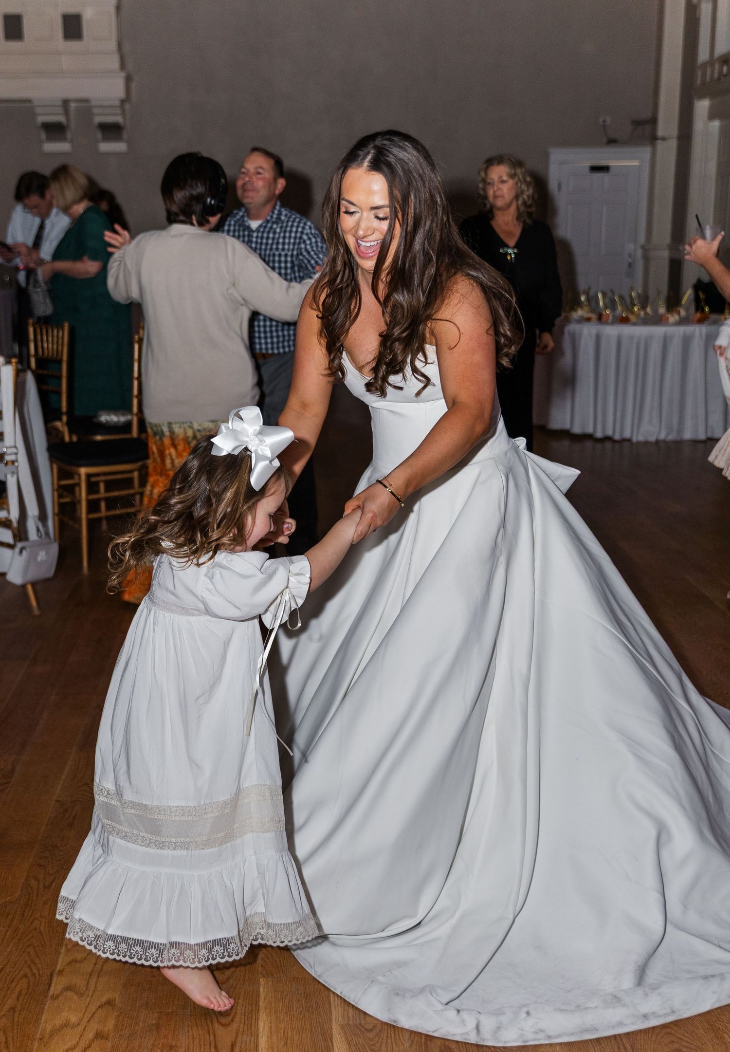 Bride in white ball gown dancing with young flower girl at wedding reception.
