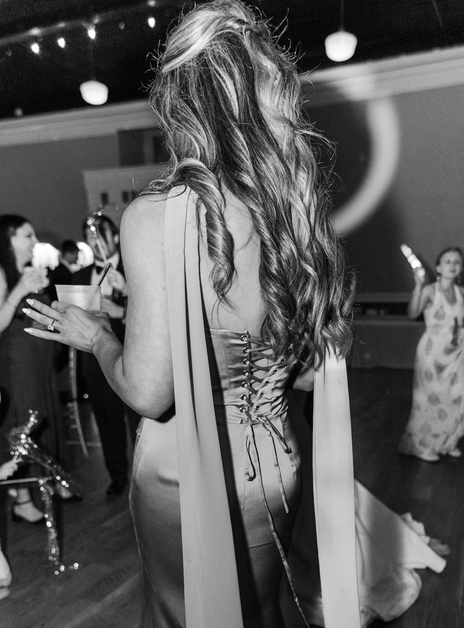 Black and white photo of bridesmaid with long wavy hair and corset-back dress dancing at reception.