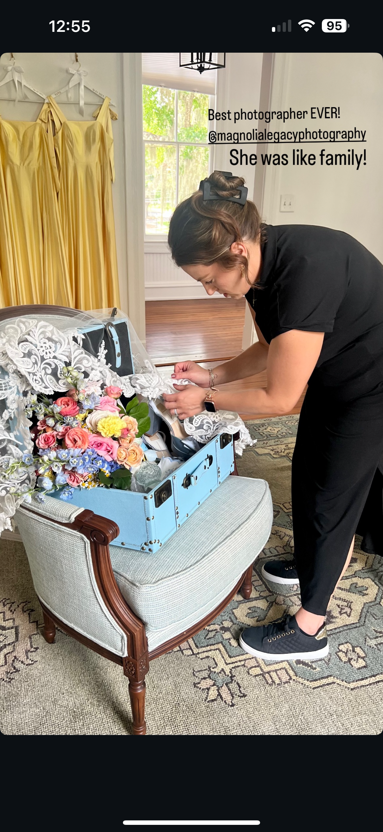 A person arranges flowers in a light blue bassinet while preparing a photography setup on a patterned rug.