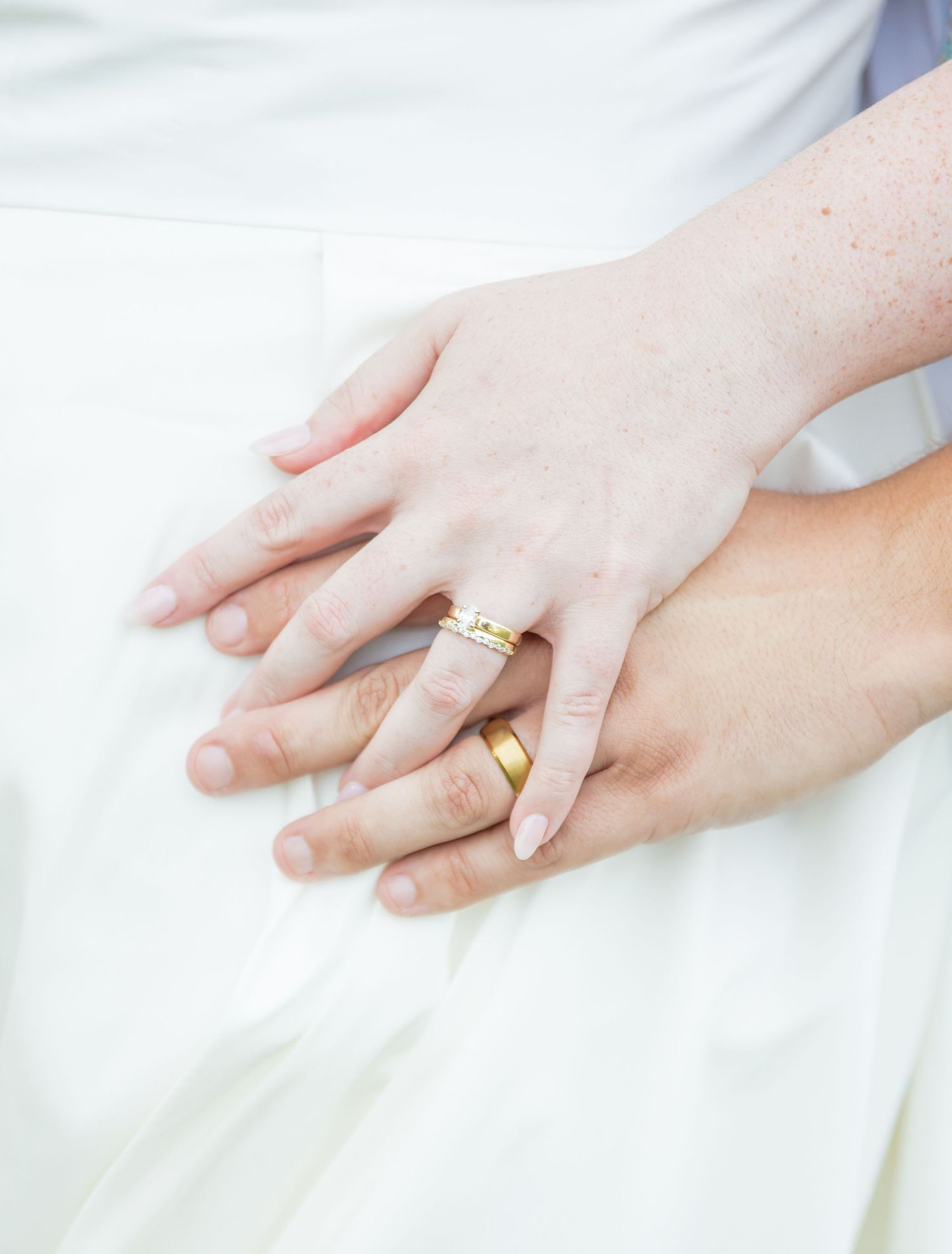 Close-up view of hands wearing white gold and diamond engagement rings against a white background.