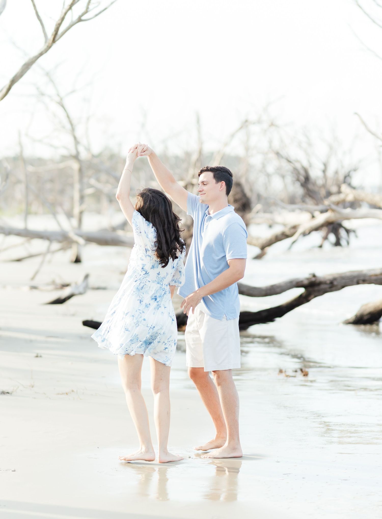Couple playing and sharing joyful moments on a beach with driftwood and water.