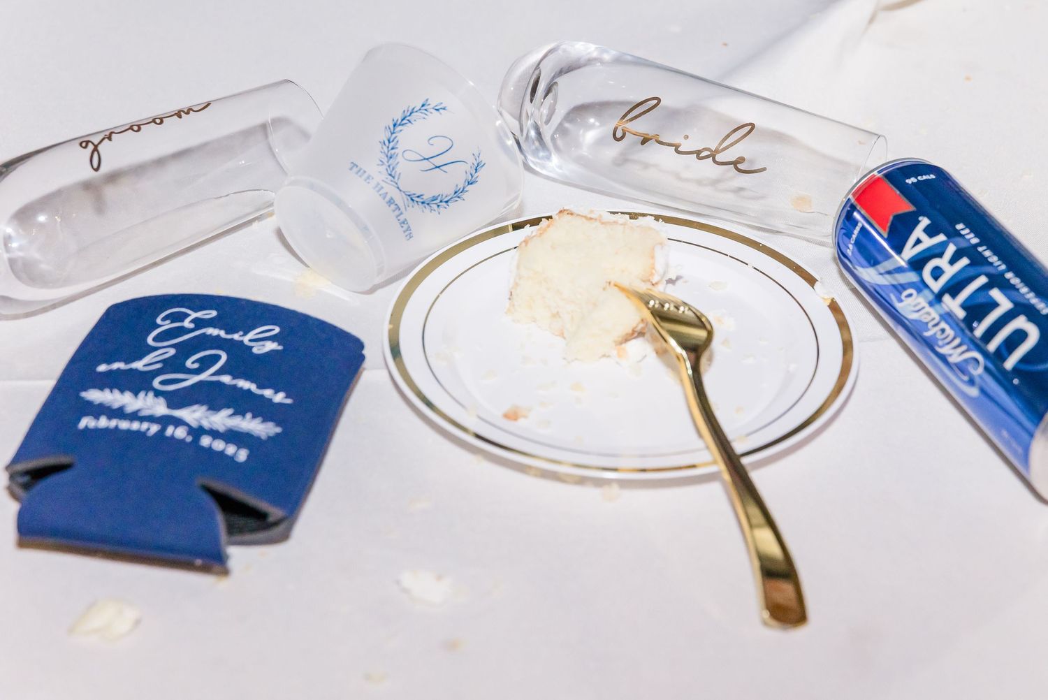Assorted party favors and accessories including white plates, plastic cups, and blue drink koozies laid out on a surface.