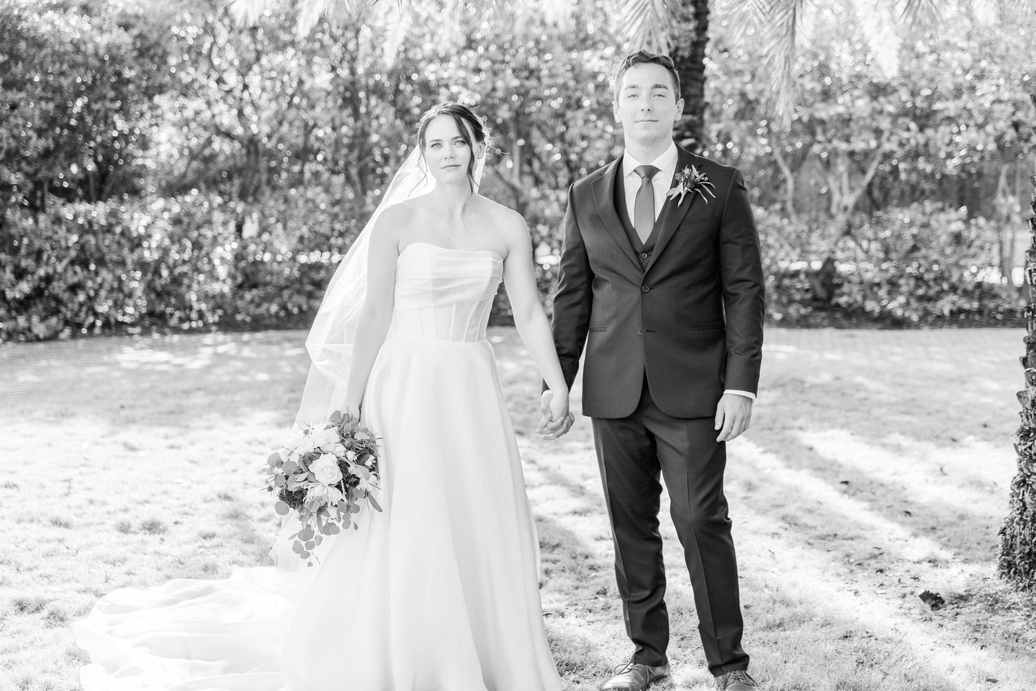 Black and white candid photo of newlyweds walking together outdoors during their wedding day.