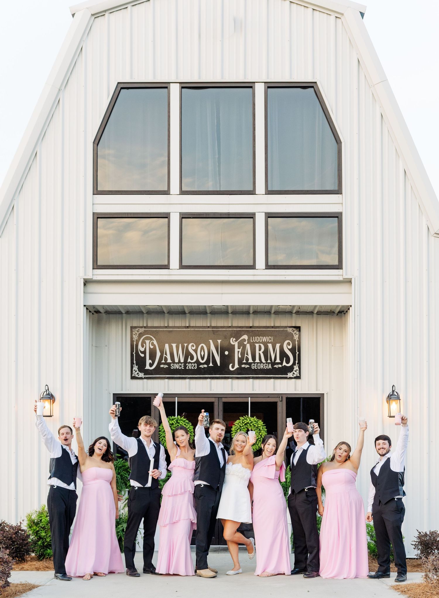 Wedding party celebrating outside Dawson Farms venue, bridesmaids in pink gowns and groomsmen in vests cheering with arms raised.