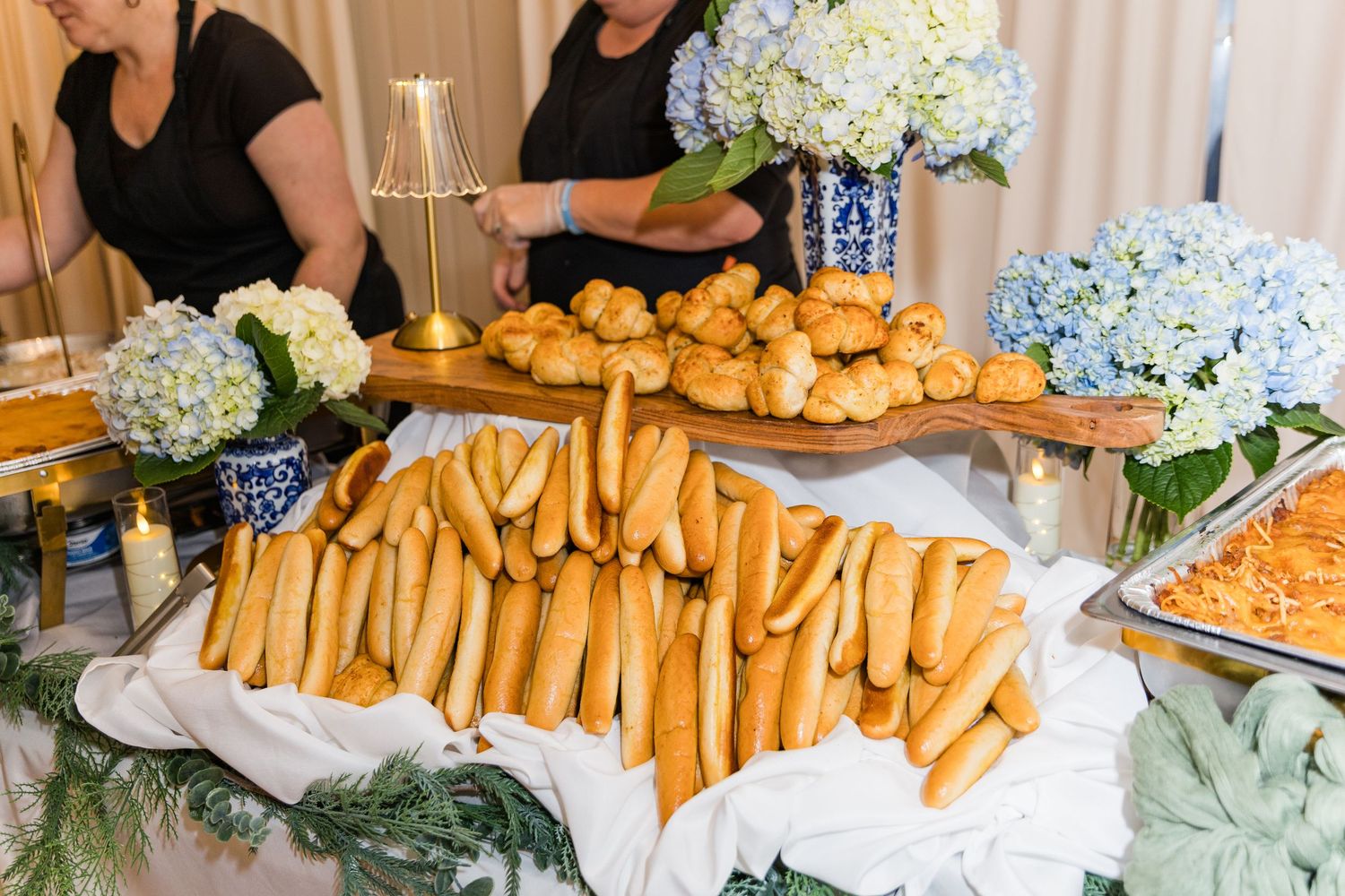 Wedding reception buffet table with breadsticks, rolls, and blue hydrangea floral arrangements.