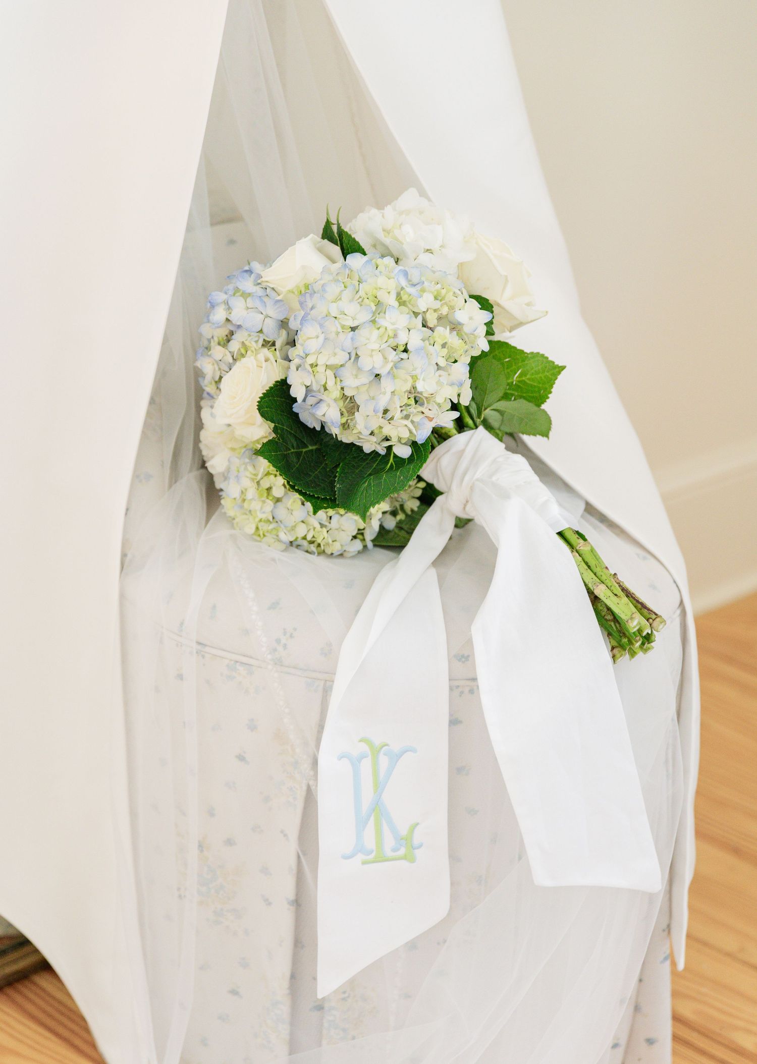 Elegant wedding bouquet of blue and white hydrangeas with monogrammed ribbon tied to a white chair.