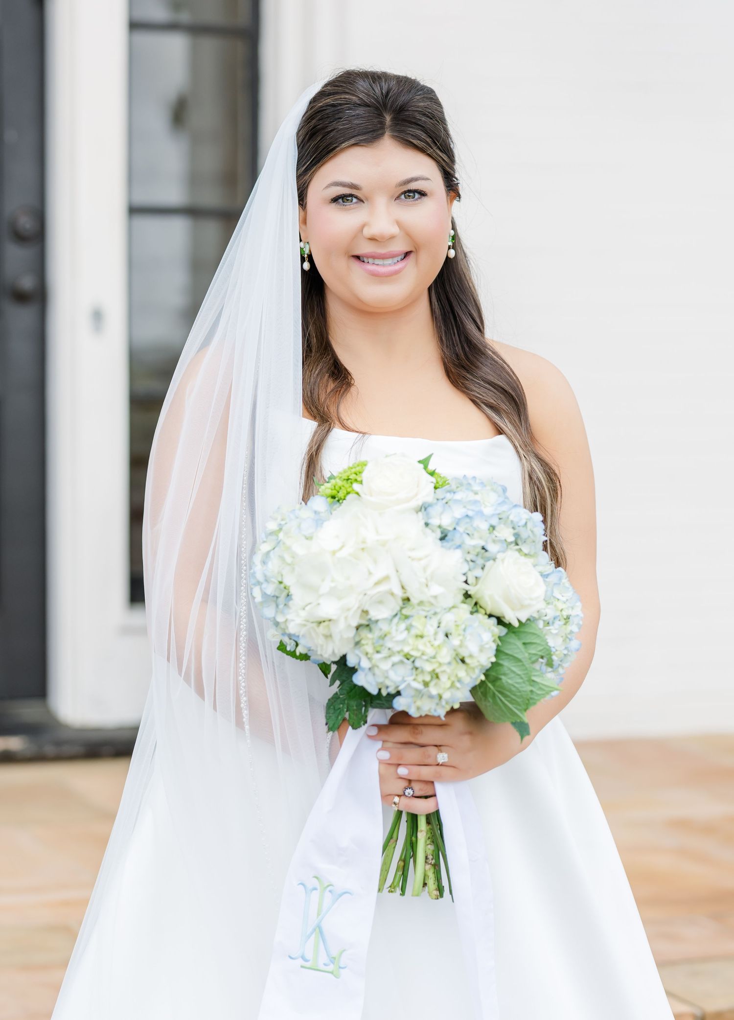 Beautiful bride in strapless white gown holding blue hydrangea and white rose bridal bouquet.