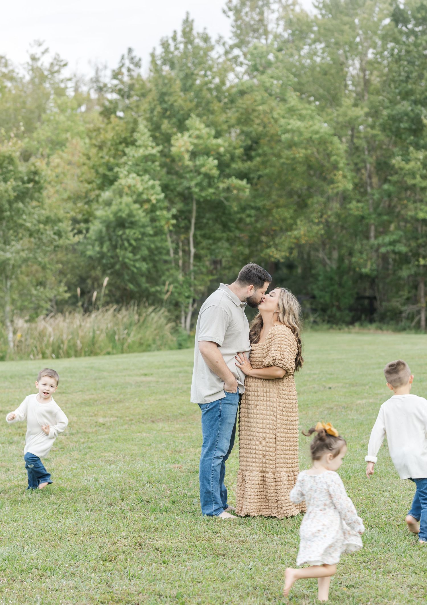A family plays together in a grassy field surrounded by trees on a sunny day.