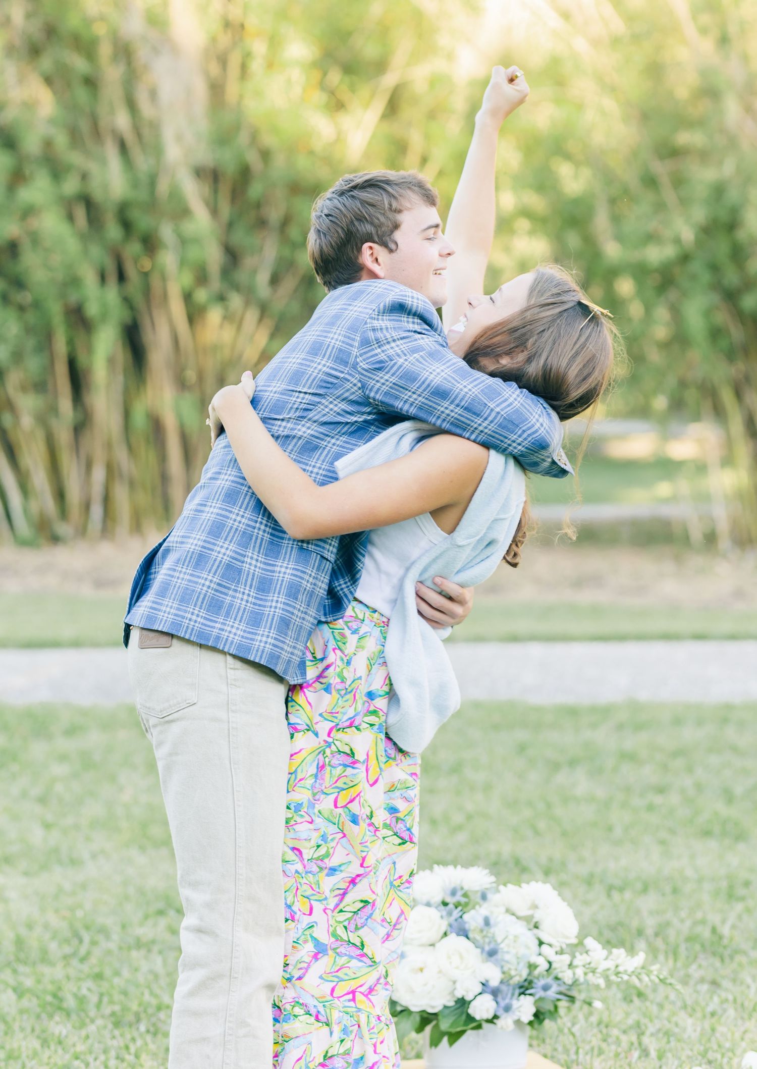 A joyful couple embraces in an outdoor setting with green foliage and white flowers in the background.
