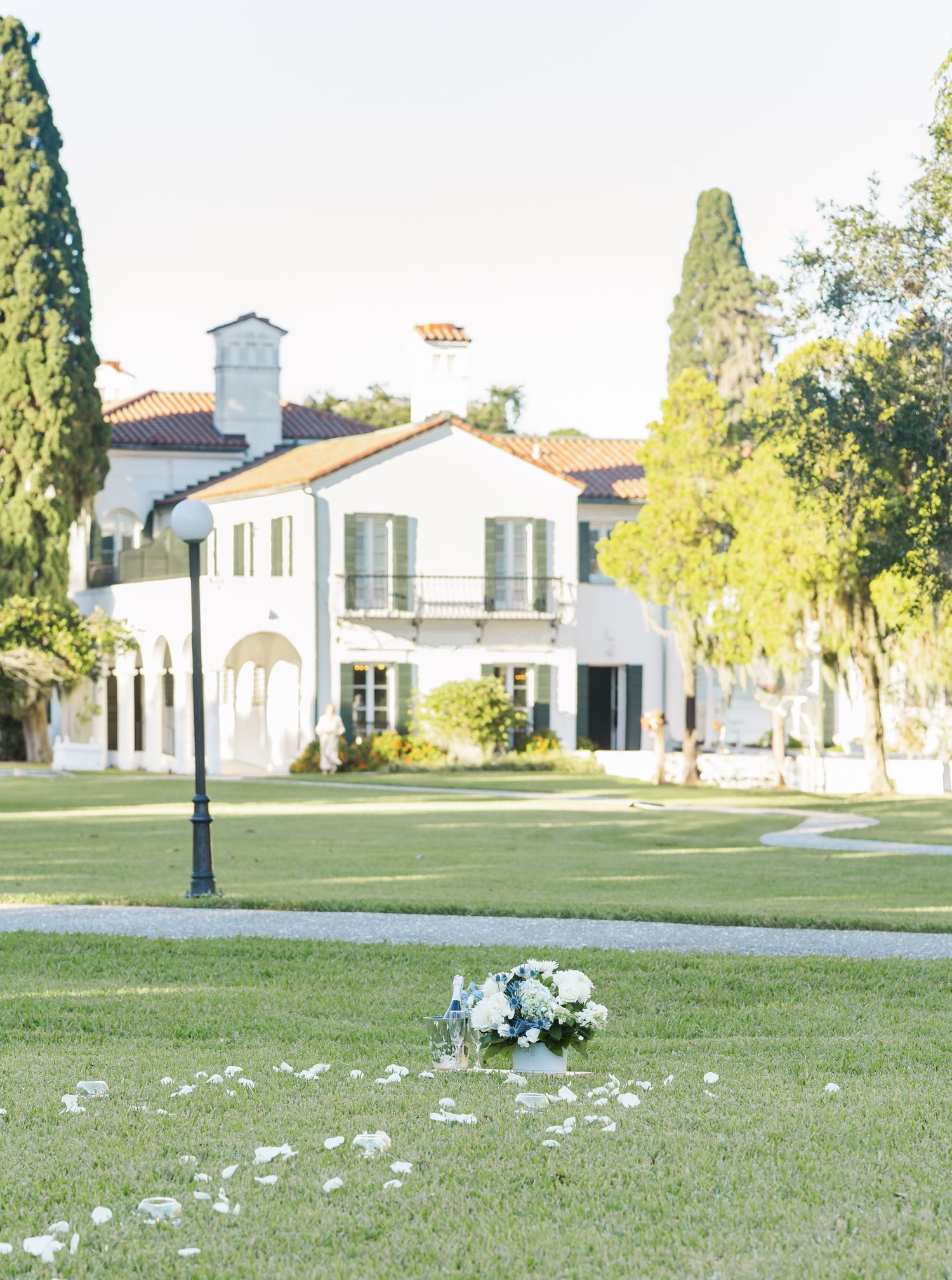 White Spanish-style buildings with terracotta roofs sit on a manicured lawn with scattered flower petals creating a romantic scene.