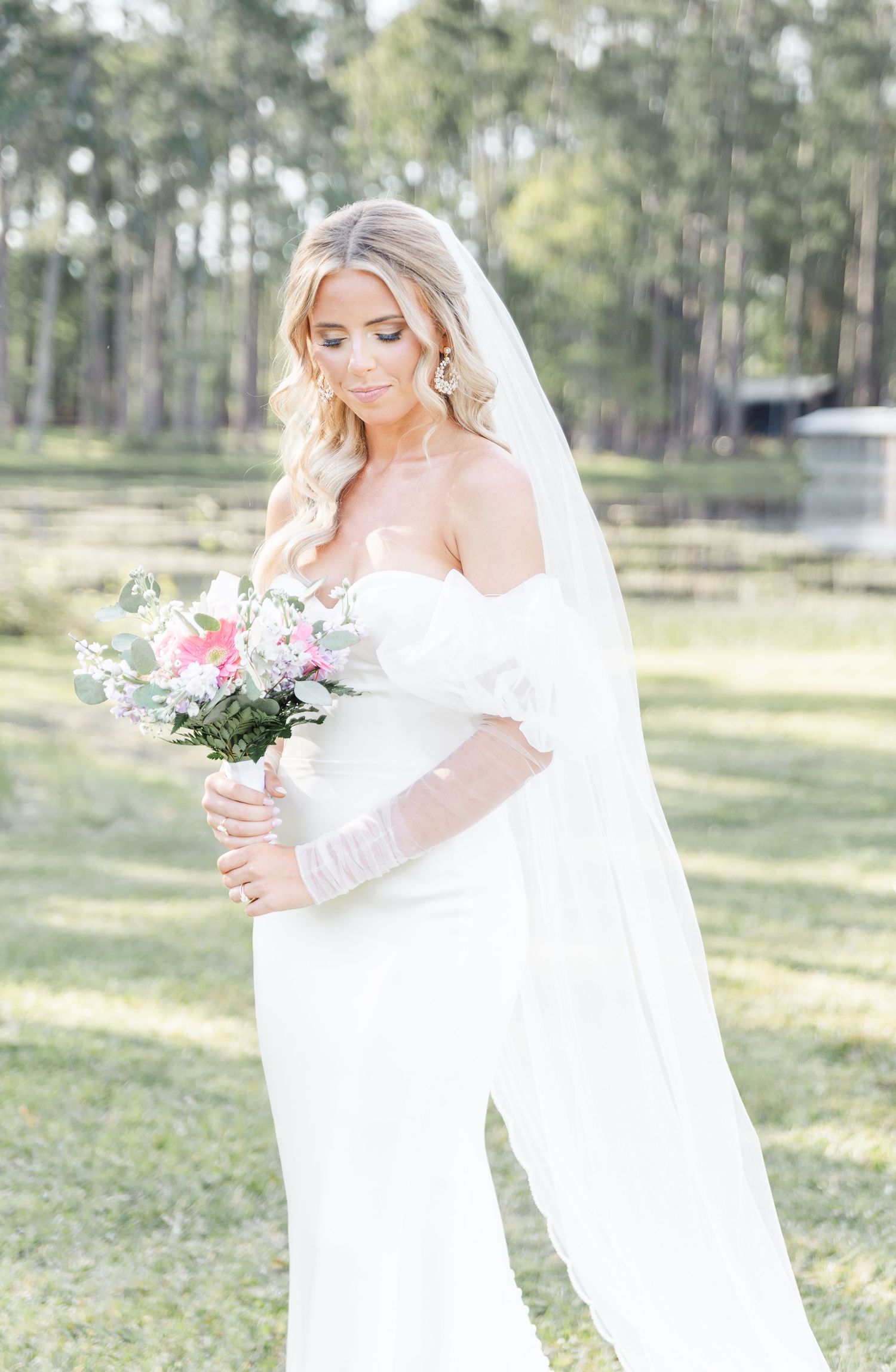 Side profile of bride in white dress holding bouquet against wooded landscape.