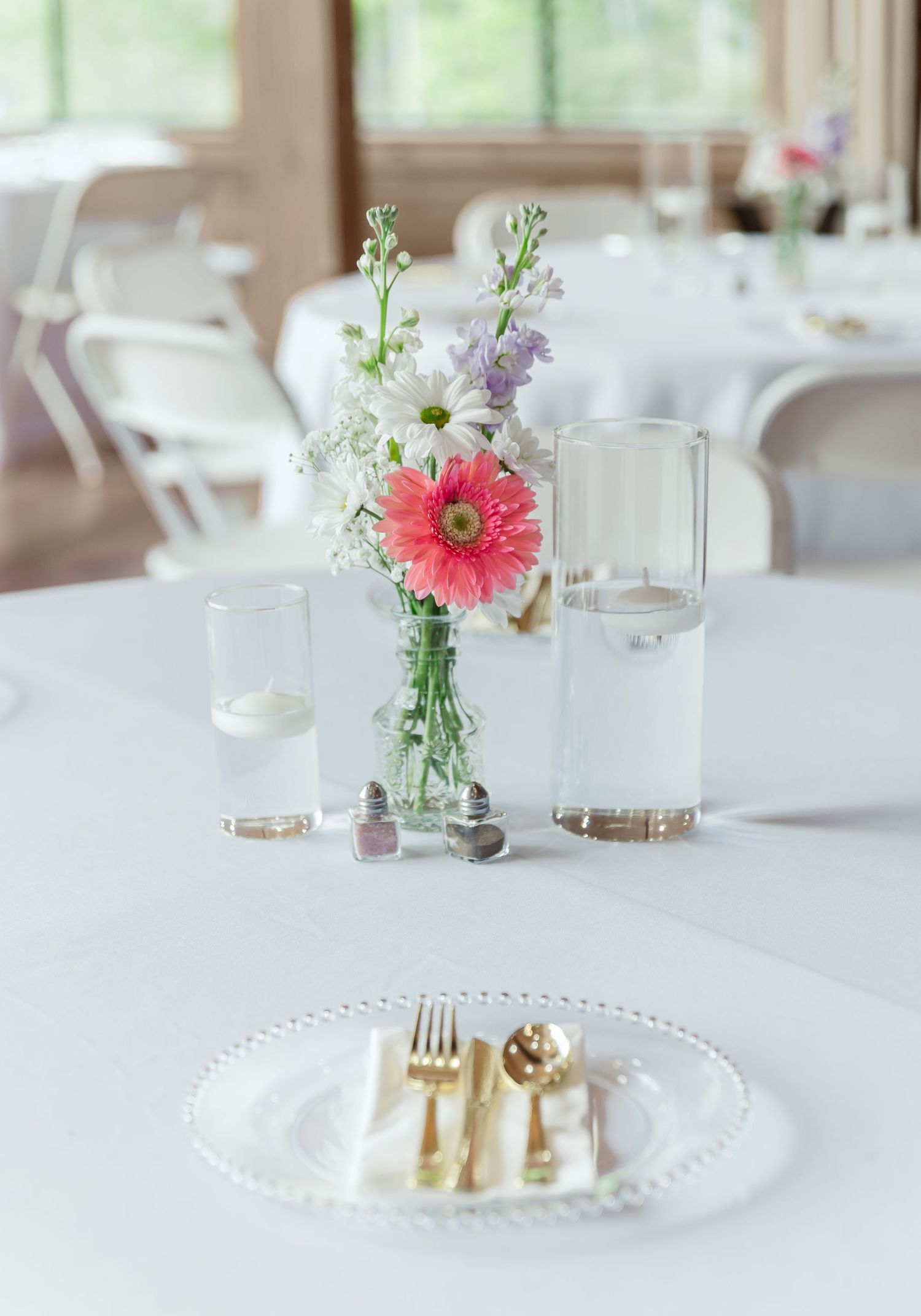 Wedding table setting with floral centerpiece, gold cutlery, and white plate.