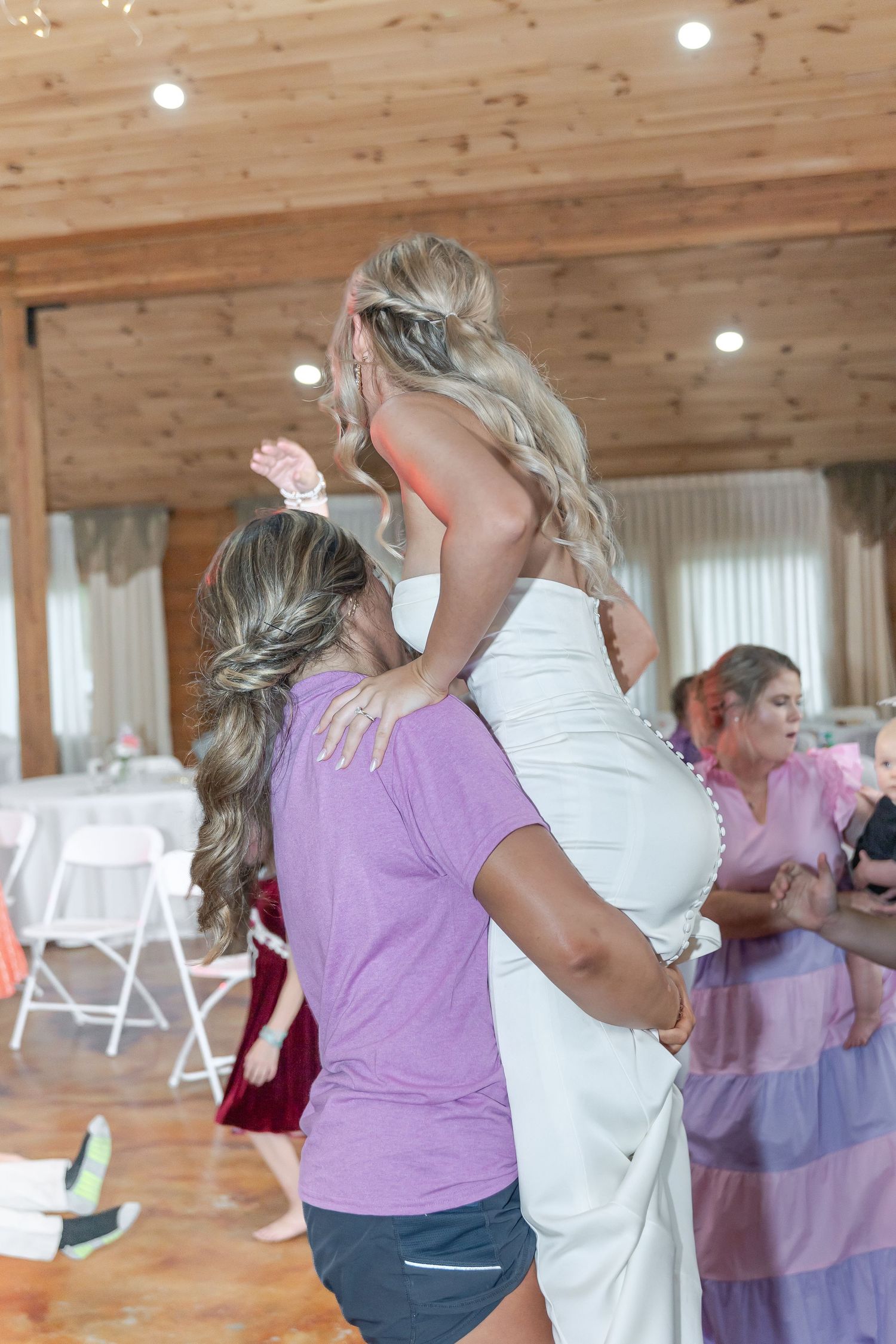 Wedding celebration dance with guests in a wooden-beamed reception hall.