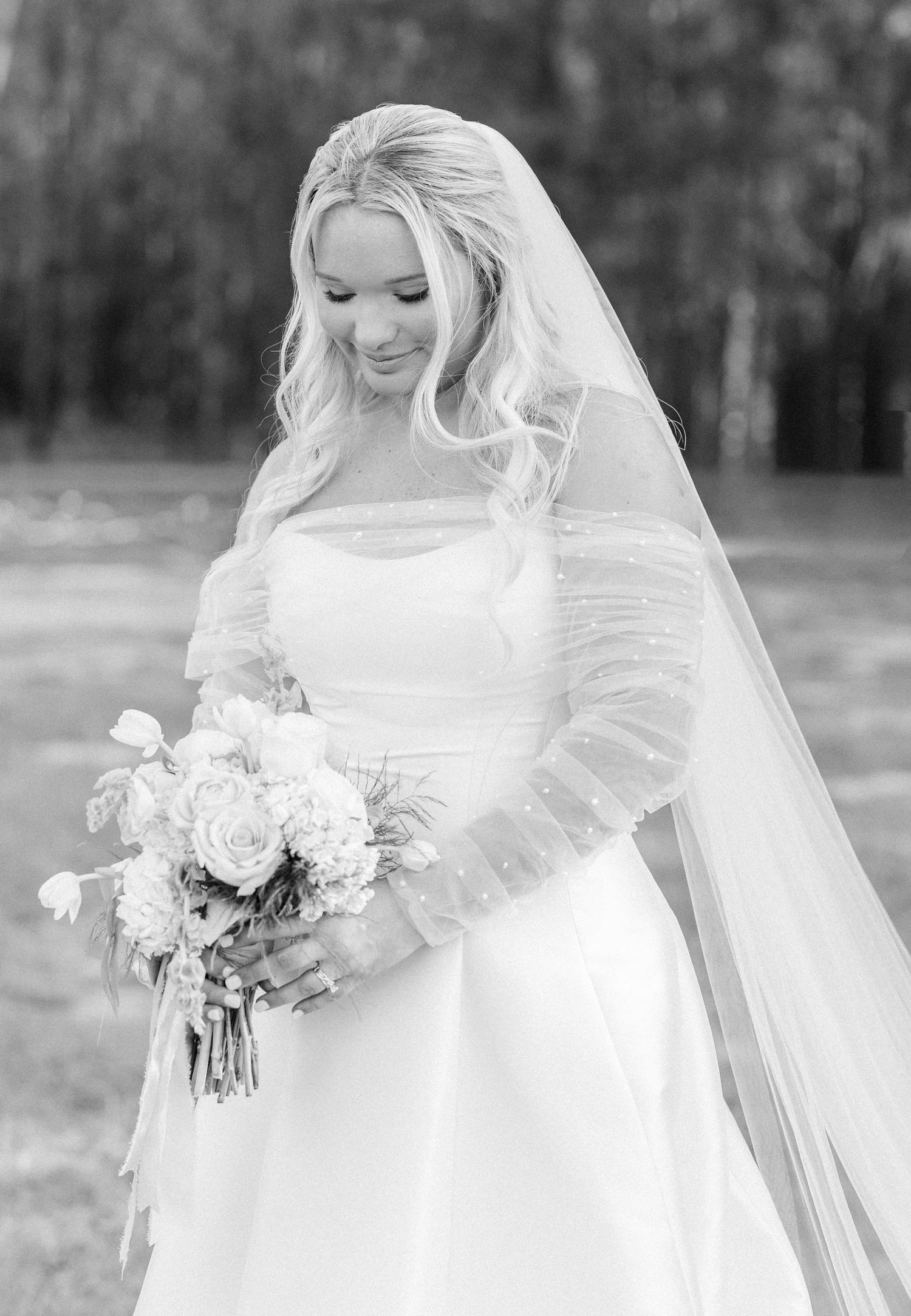Black and white portrait of a smiling bride in a lace bolero holding a white rose bouquet with flowing veil.