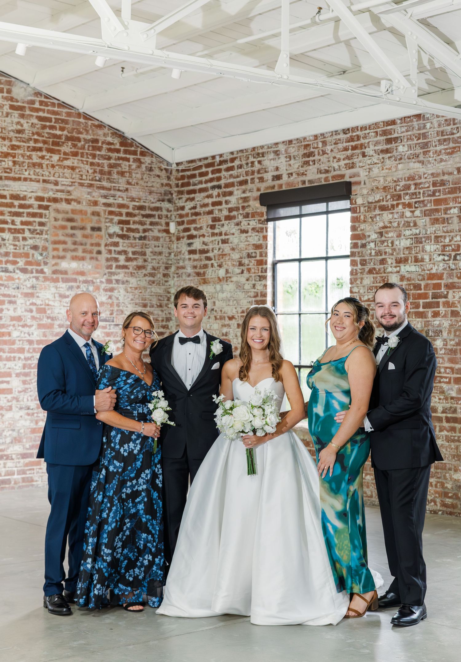 Bride and groom celebrate with family of four in colorful formal attire at brick venue.