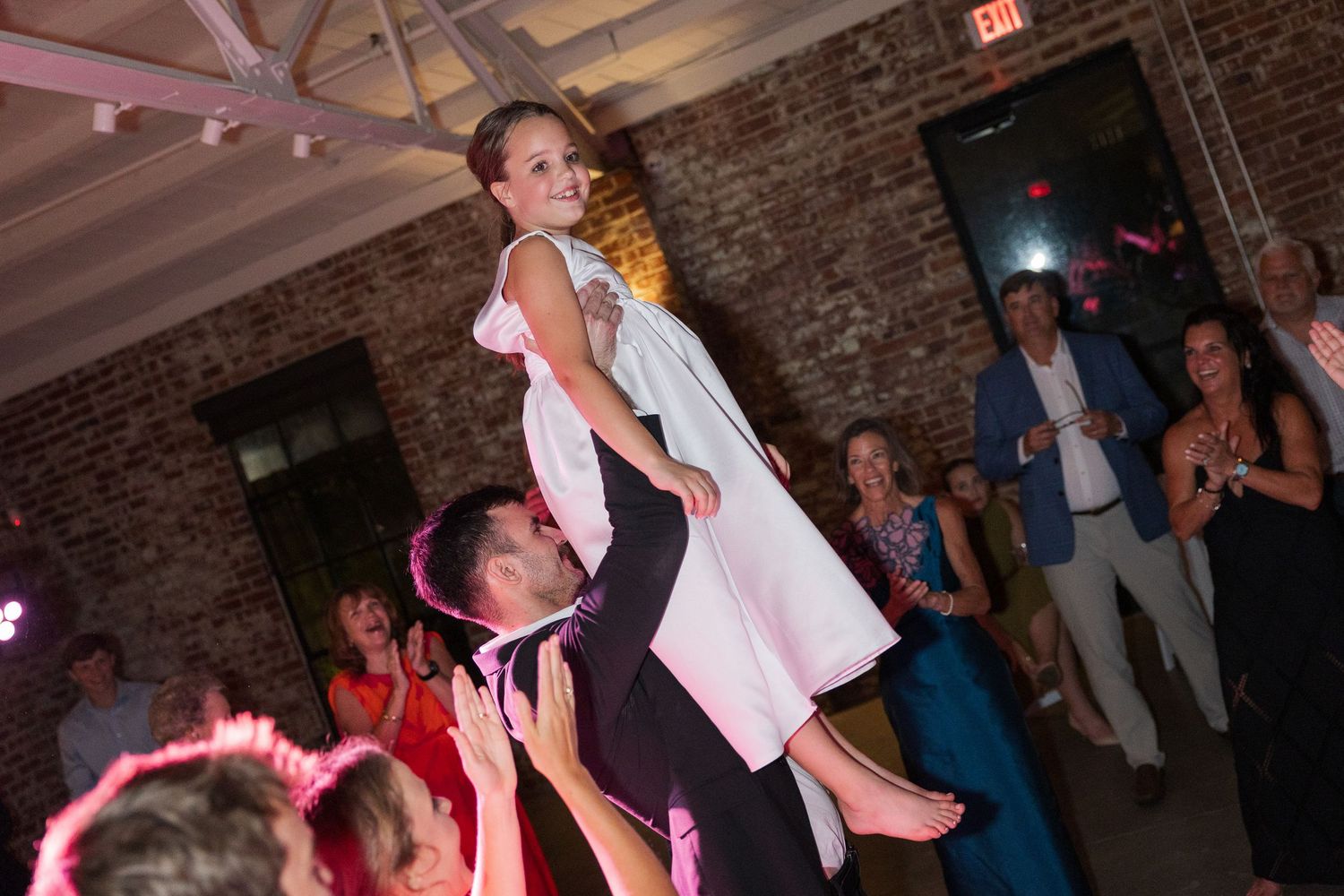 Groom lifting bride in white dress above dance floor at lively wedding reception.