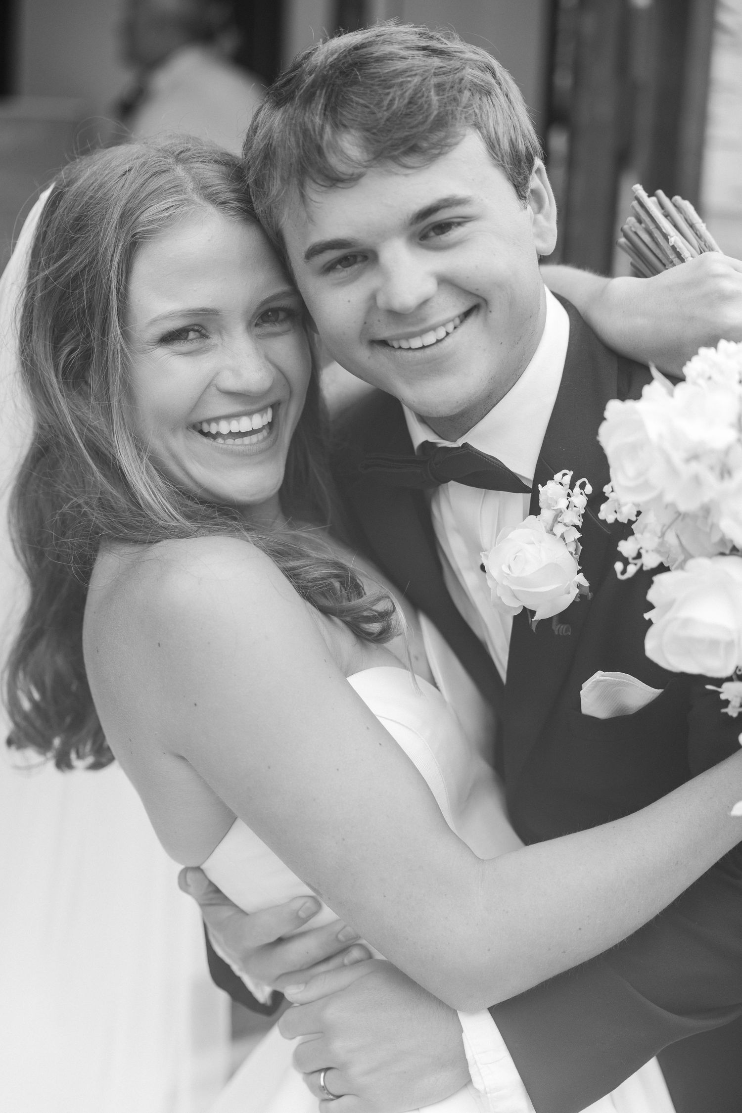 Happy bride and groom embrace and smile together in black and white wedding portrait.