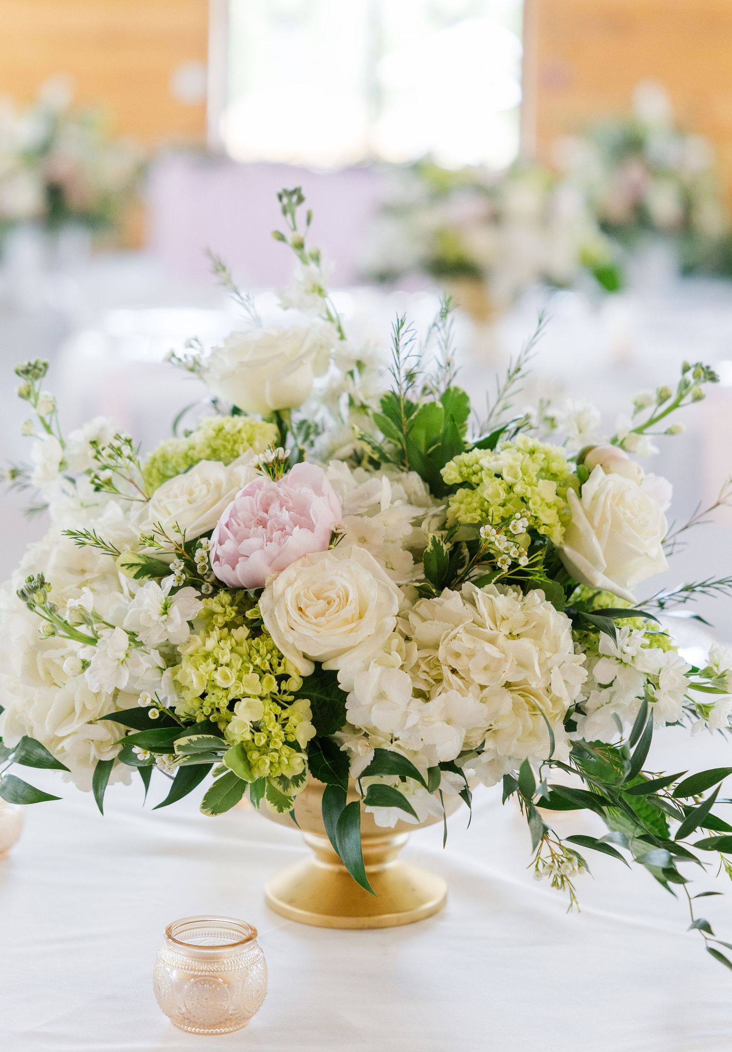 Elegant wedding centerpiece with white roses, pink peonies, and green hydrangeas in a gold urn vase.
