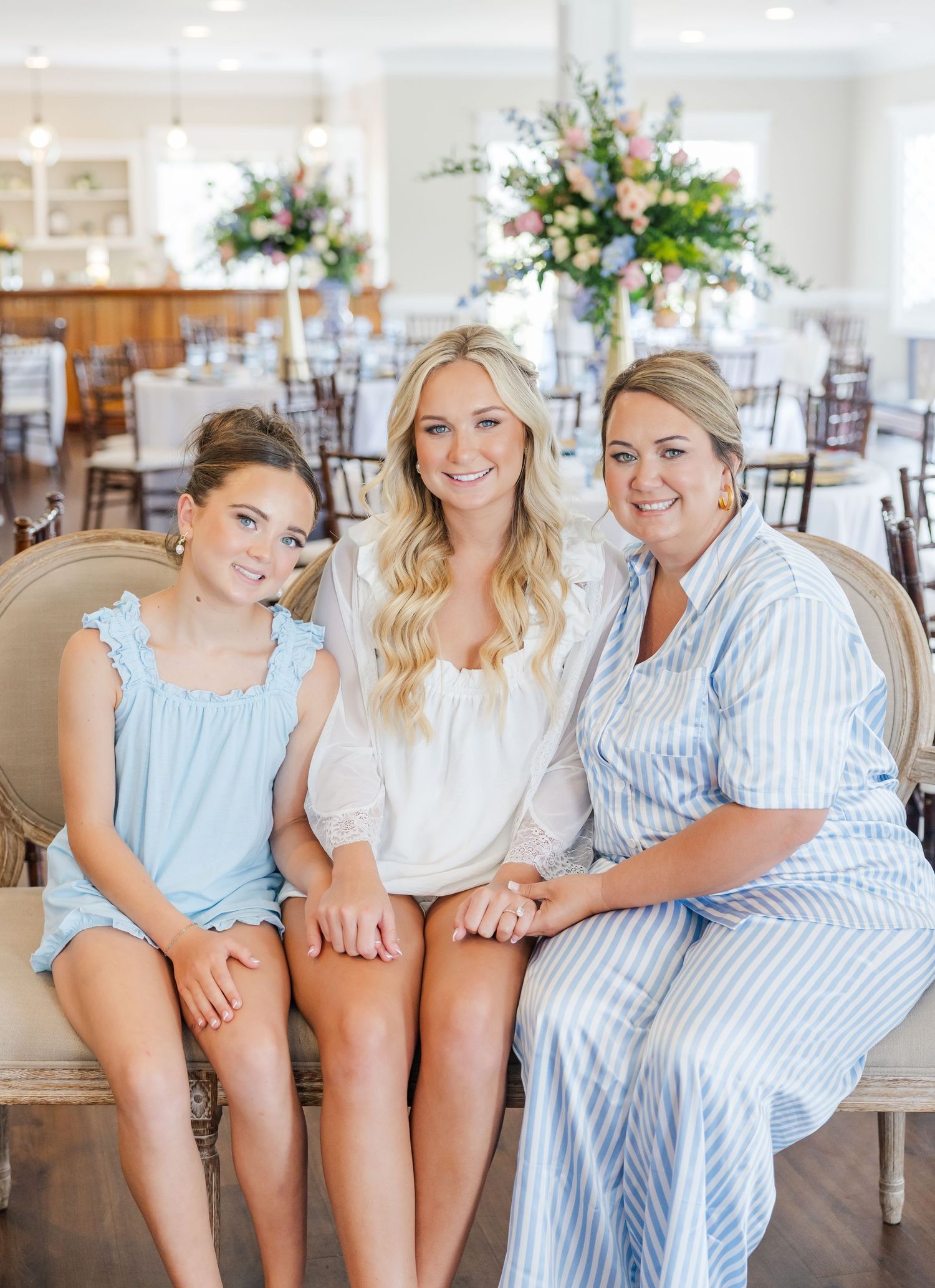 Bride in white top poses with young girl in blue dress and woman in striped outfit at wedding reception venue.