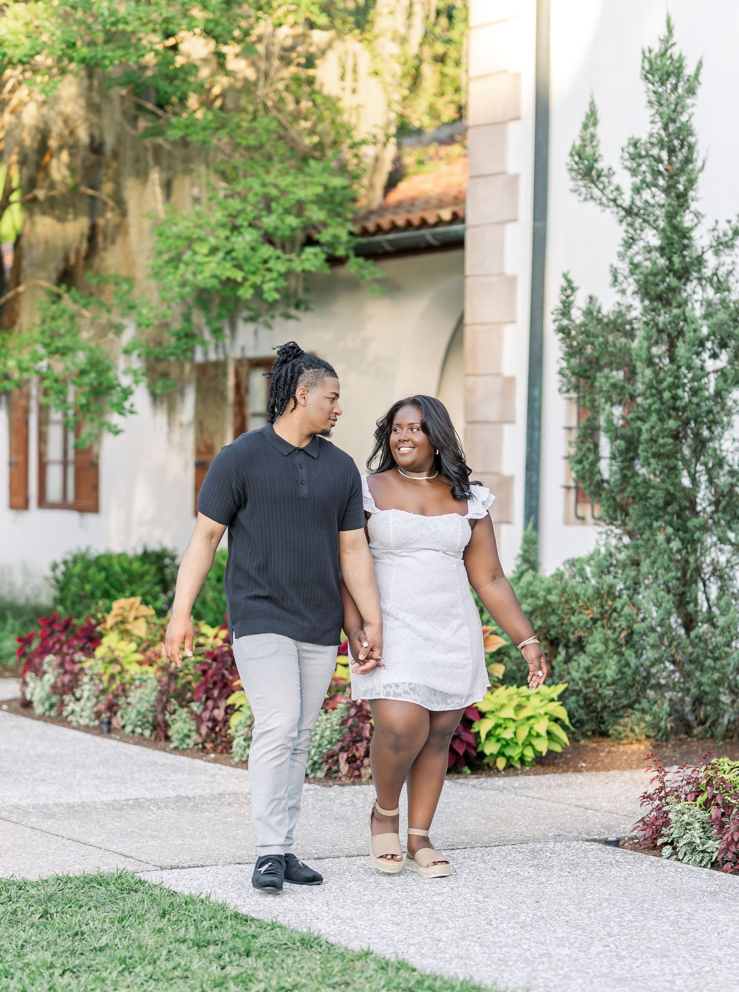 A couple strolling hand in hand through a landscaped garden with flowering plants and stone pathways.
