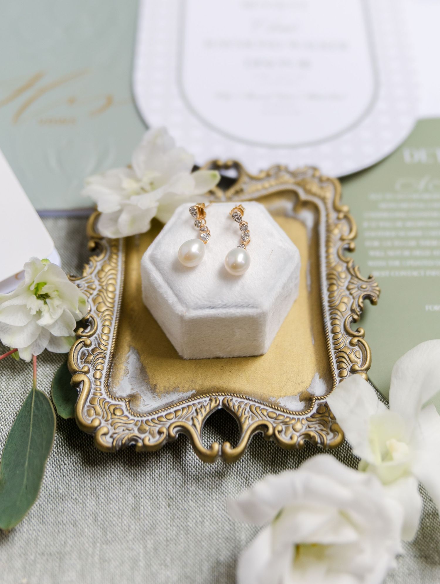 Wedding jewelry and accessories styled on vintage gold frames with white flowers and pearl details.