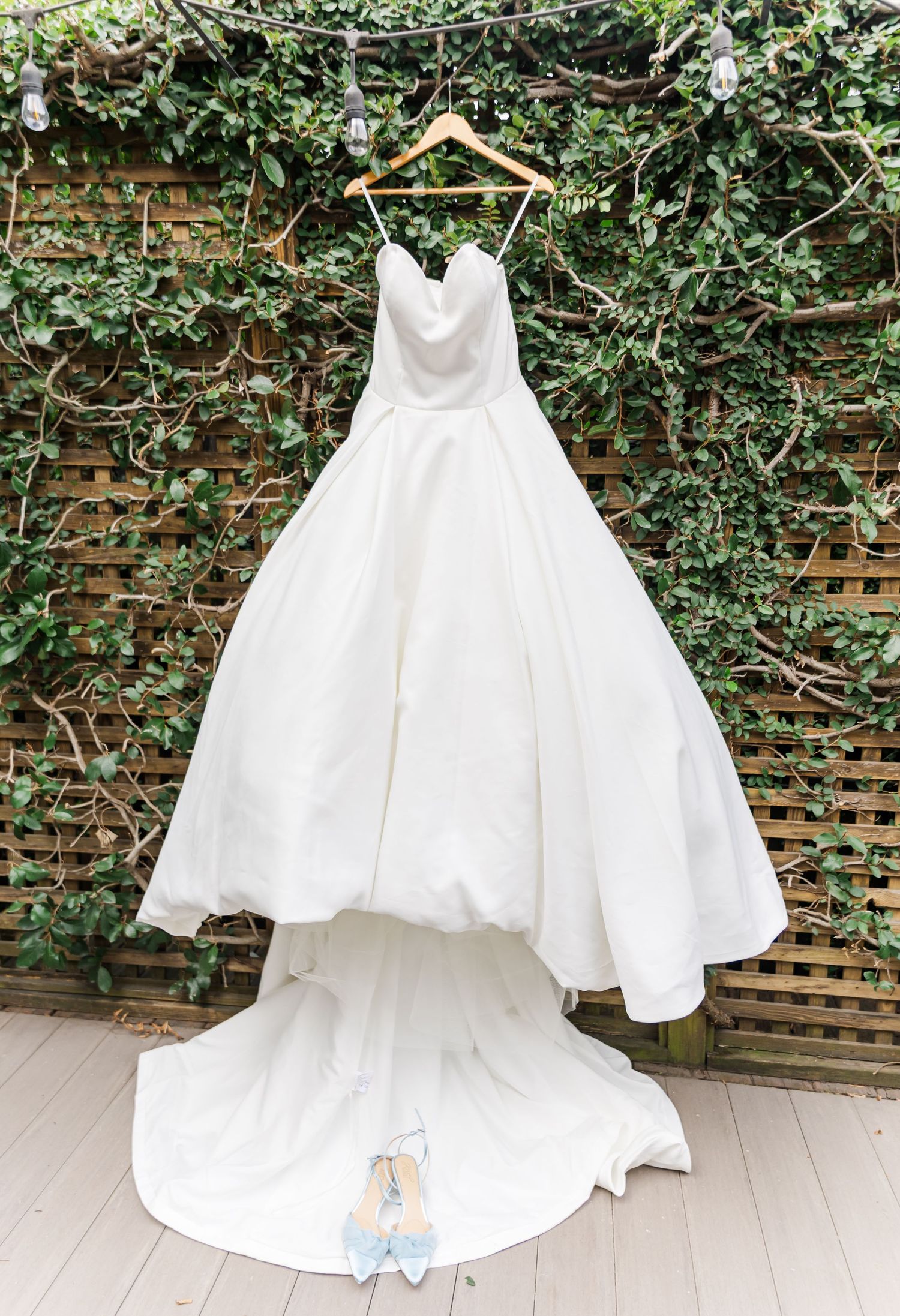 White wedding and flower girl dresses hanging on display against ivy covered brick wall.