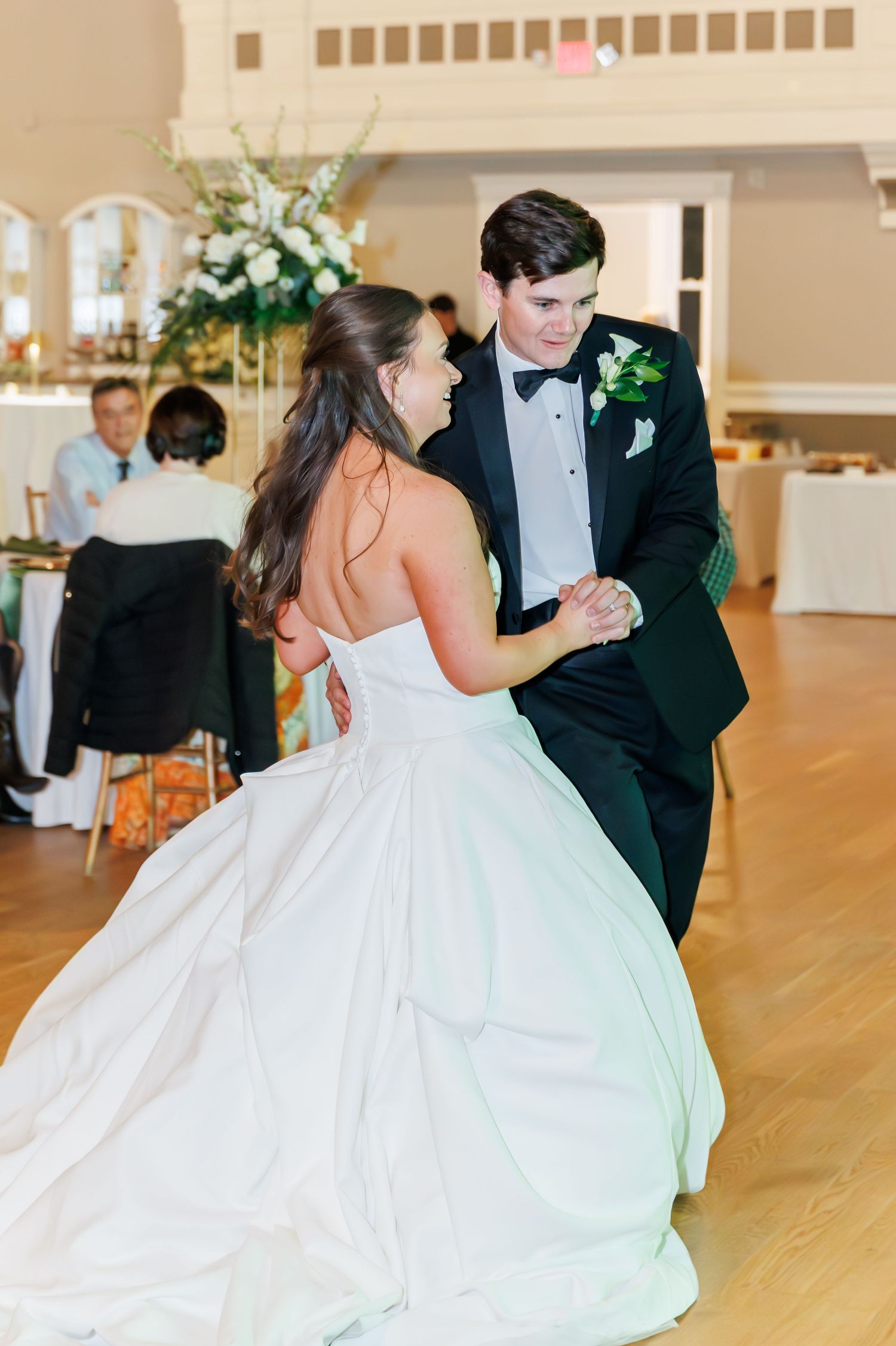 A couple shares a romantic dance on their wedding day in an elegant ballroom with wooden floors.