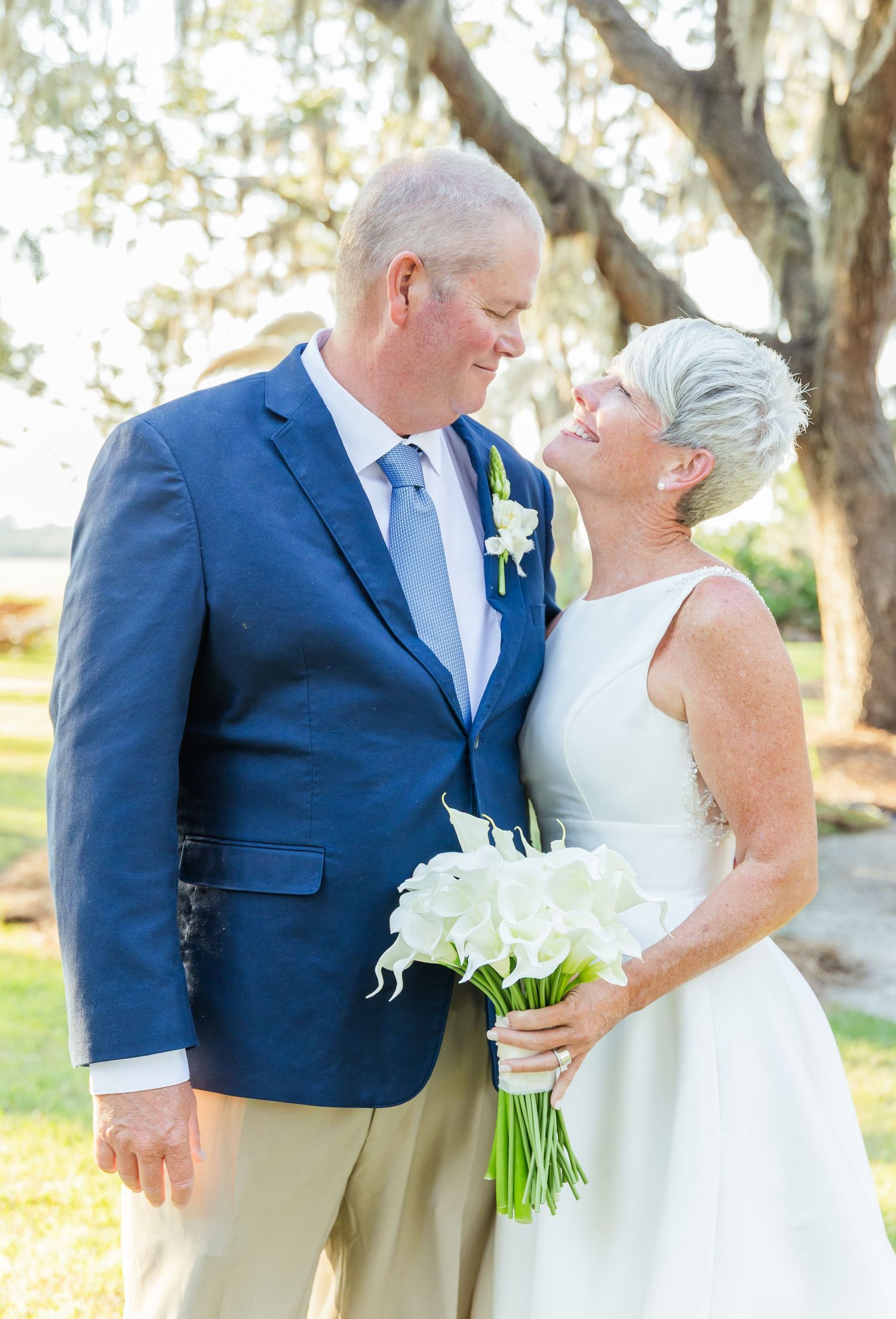 A couple shares an intimate moment in white and navy attire during their outdoor wedding ceremony.