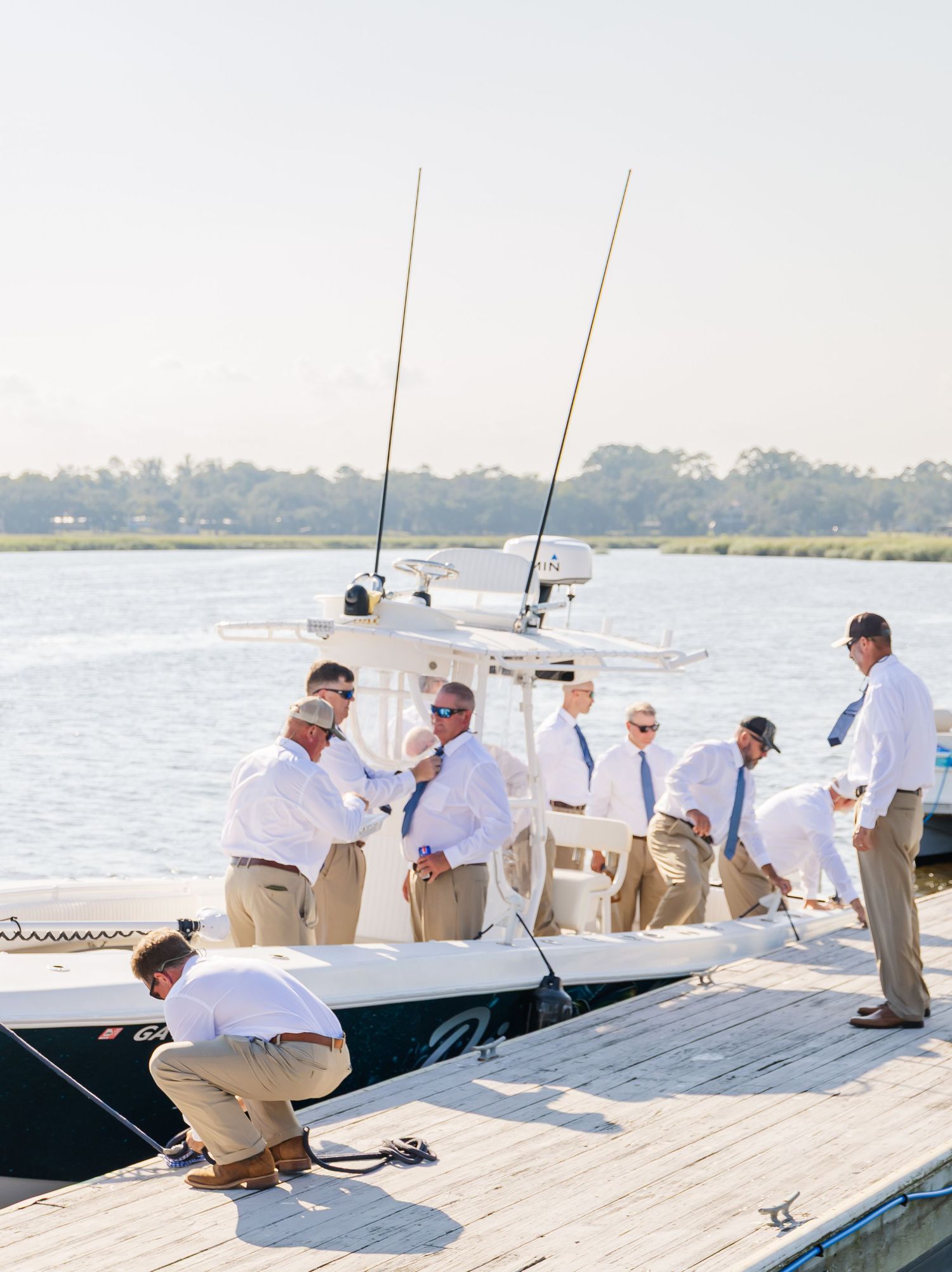 Several people in light colored clothing standing on a wooden pier beside a boat.