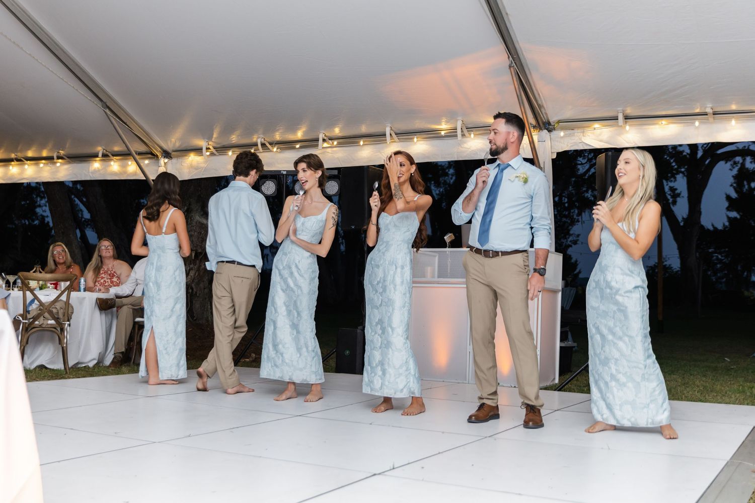 Wedding guests dancing and having fun on a white dance floor under an outdoor tent at sunset.