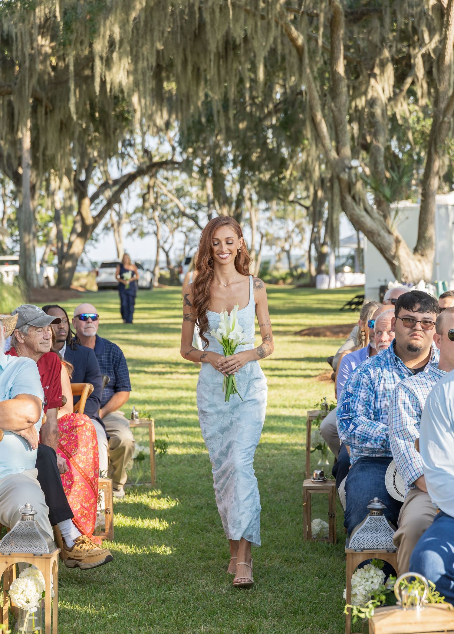 Wedding guests seated on rustic chairs beneath Spanish moss-covered trees during an outdoor ceremony.