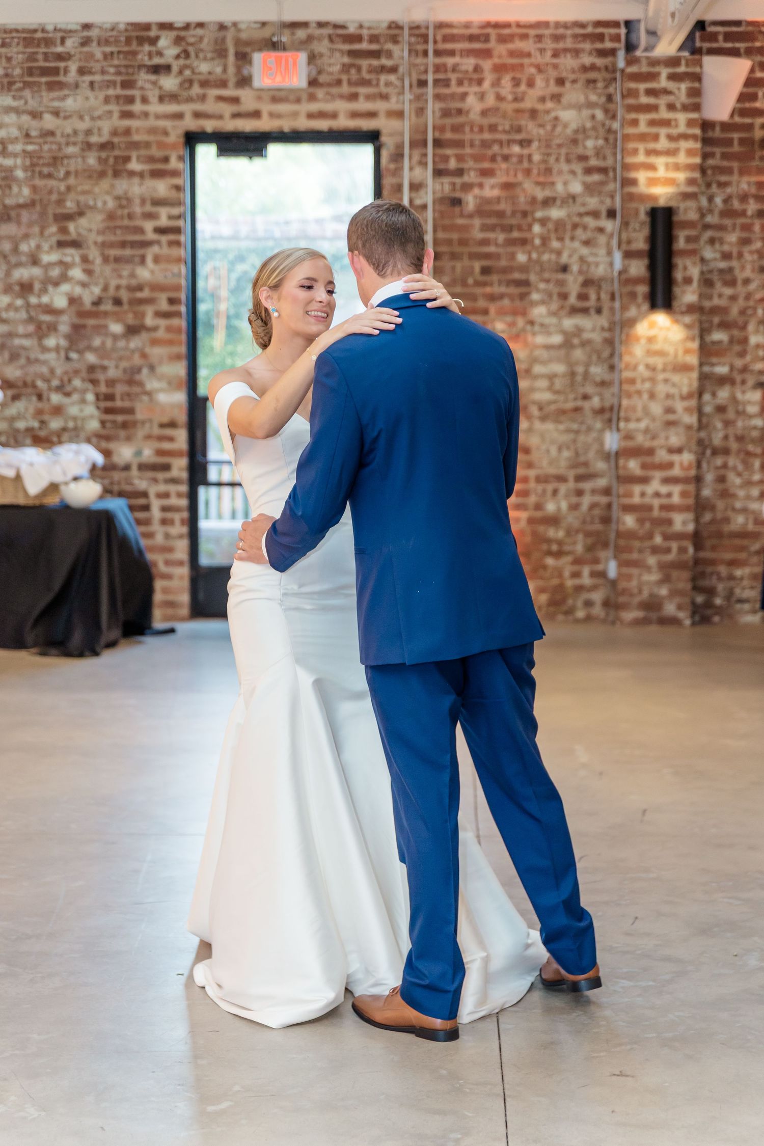 A couple shares their first dance at their wedding reception in a rustic brick-walled venue.