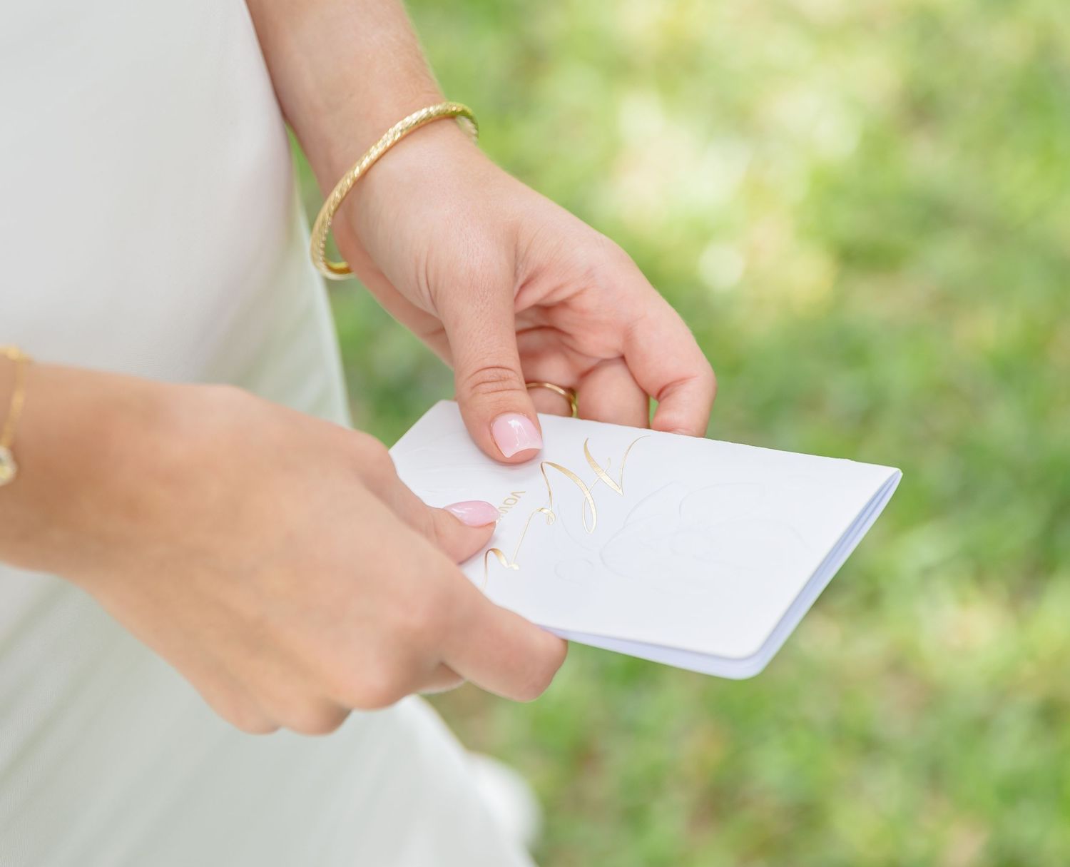 A hand holds a white business card against a blurred green outdoor background.