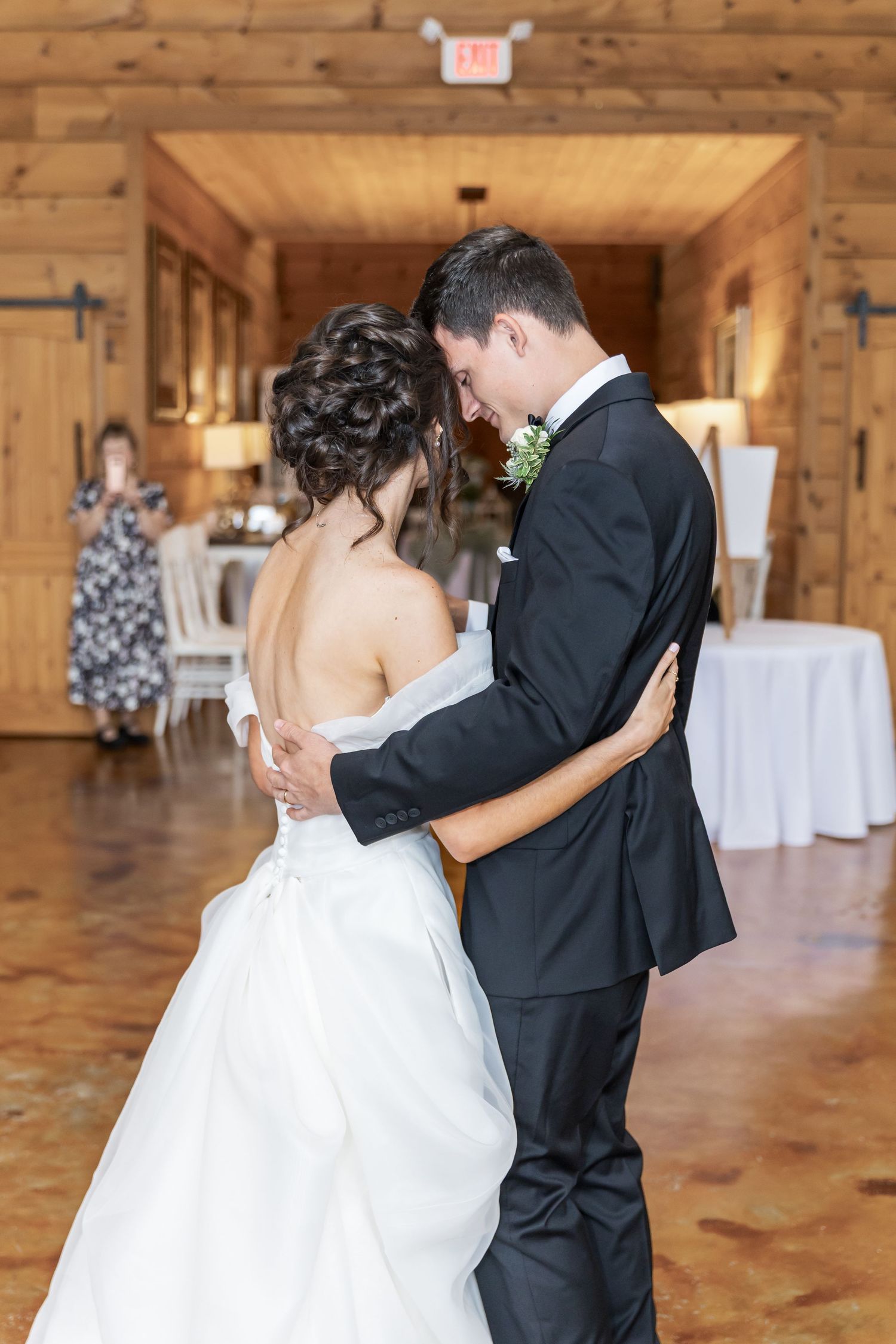 A couple shares their first dance in a rustic wooden barn venue with warm lighting and polished floors.