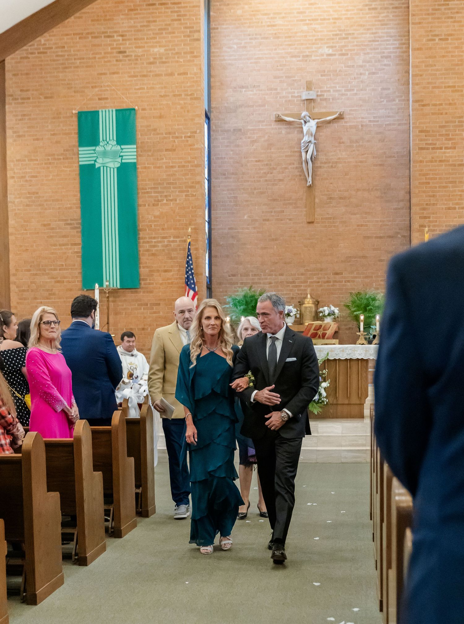 Wedding ceremony in a Catholic church with wooden pews and green accents on the walls.