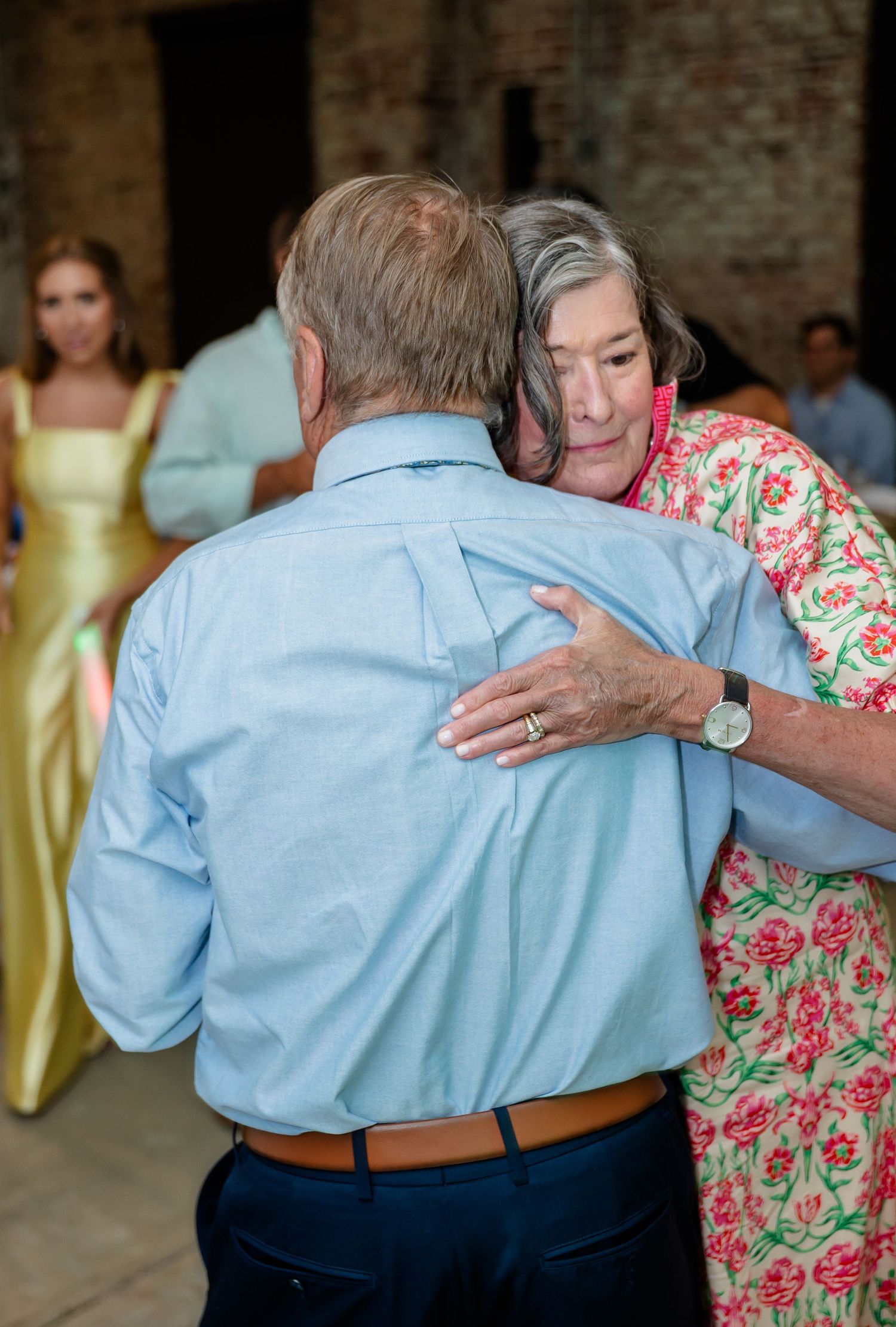 Couples slow dancing together at a wedding reception with yellow-dressed bridesmaids in background.