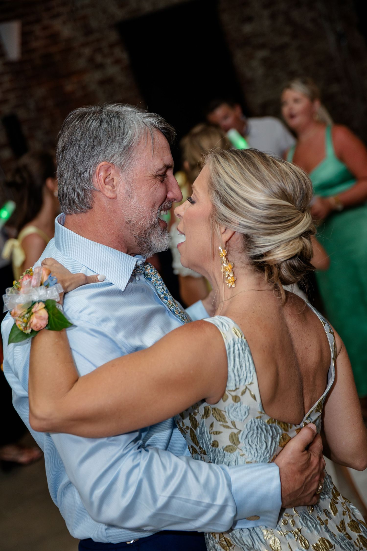 Wedding guests dance intimately in a dimly lit reception venue with brick walls and colored lighting.