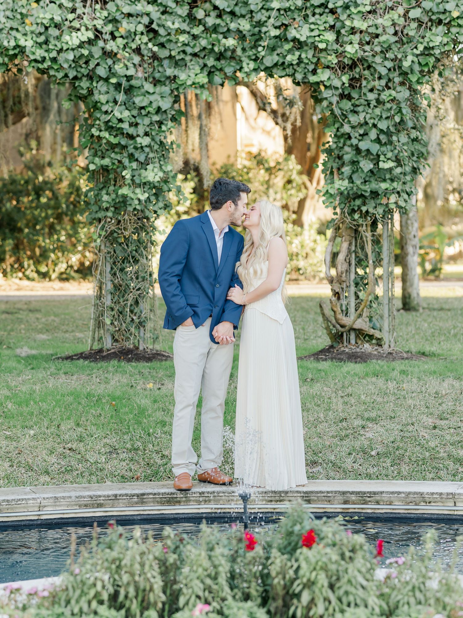 Romantic engagement photos in a garden setting with ivy-covered trees and white stone features.