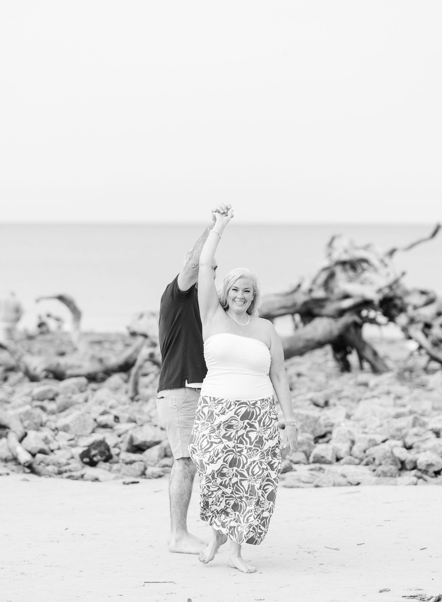 A black and white photo of two people dancing together on a beach with their arms raised in joyful celebration.