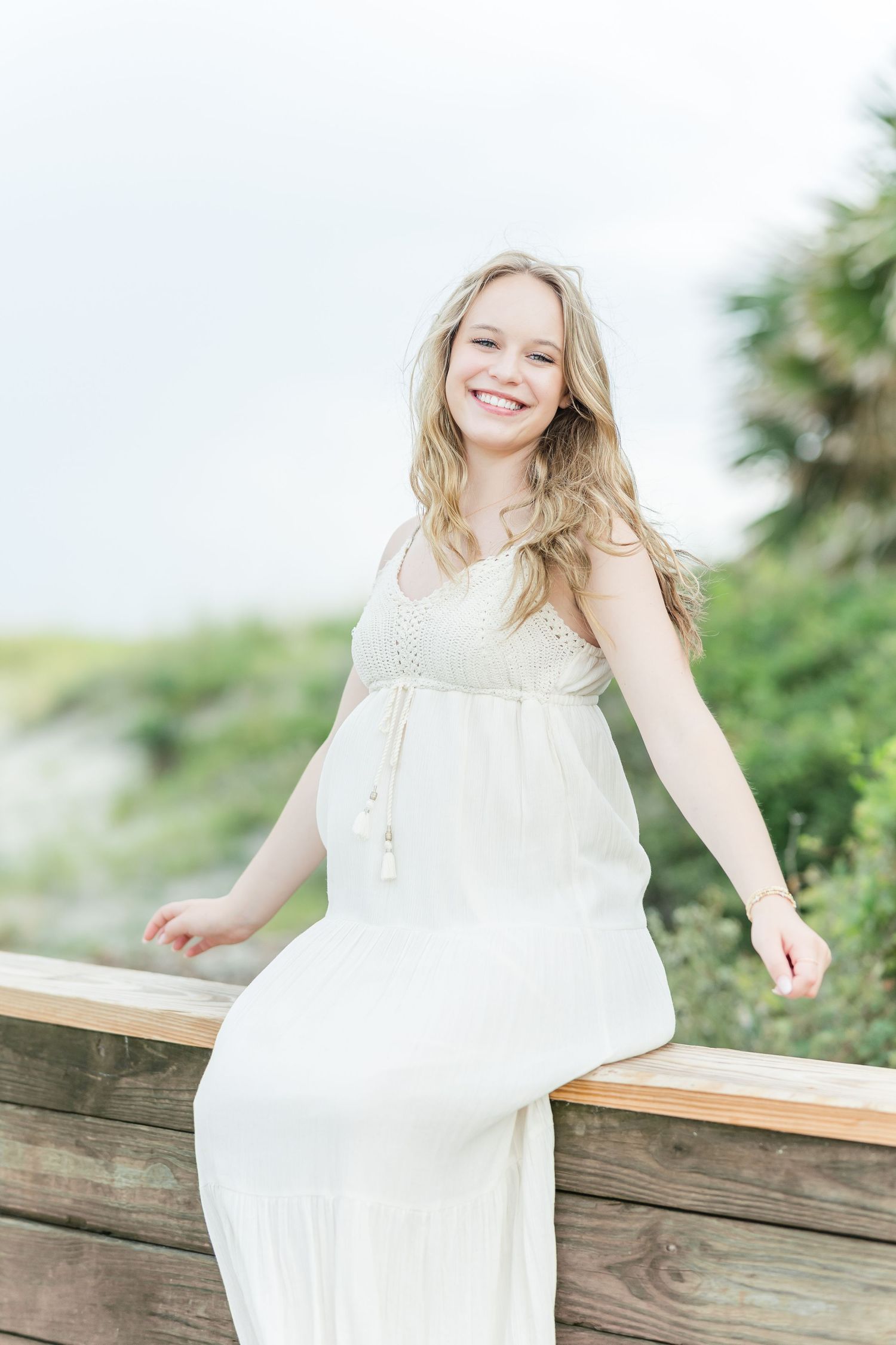 White flowy maxi dress on wooden boardwalk with tropical foliage in background.