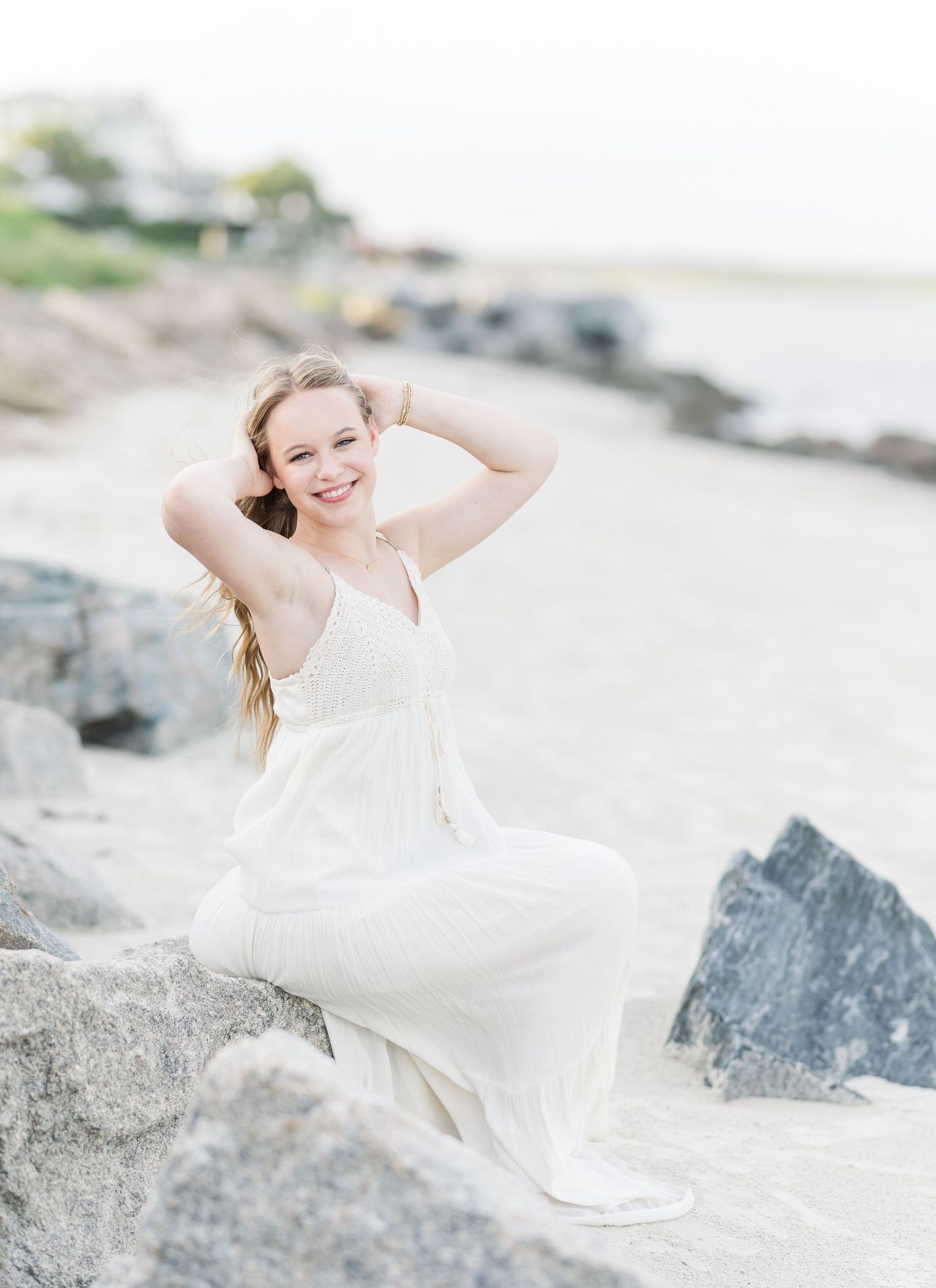 A flowing white dress creates an ethereal scene among coastal rocks at the beach.