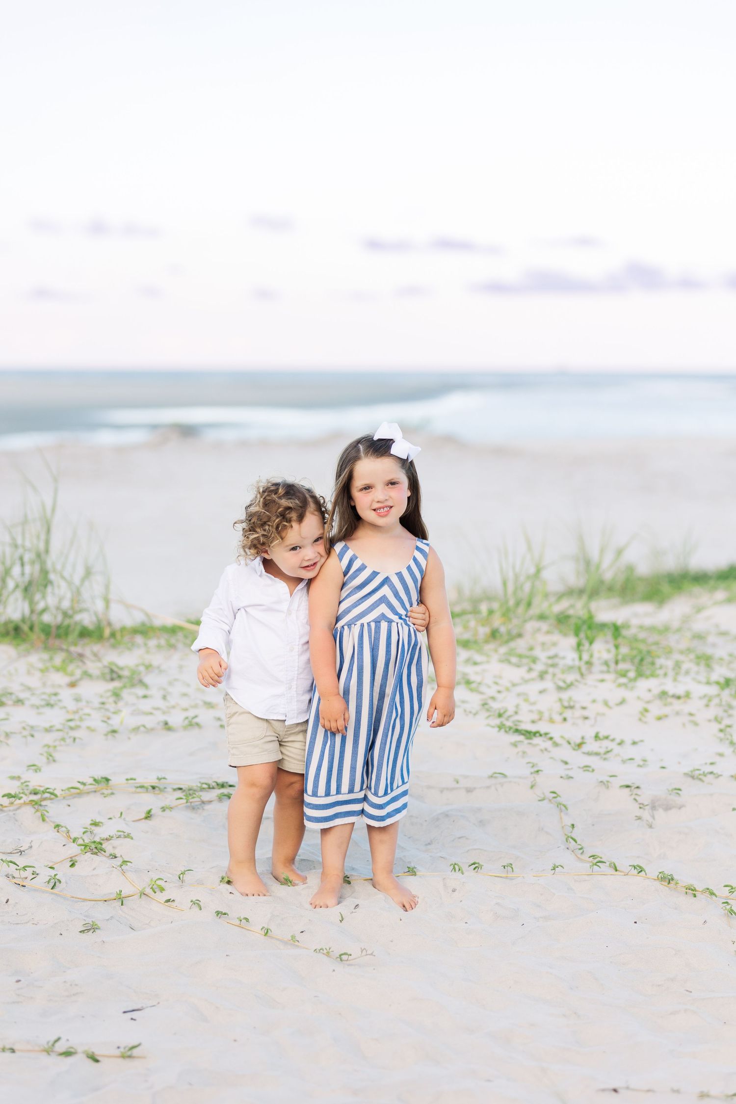 Two children playing together barefoot on a sandy beach with ocean waves in the background.