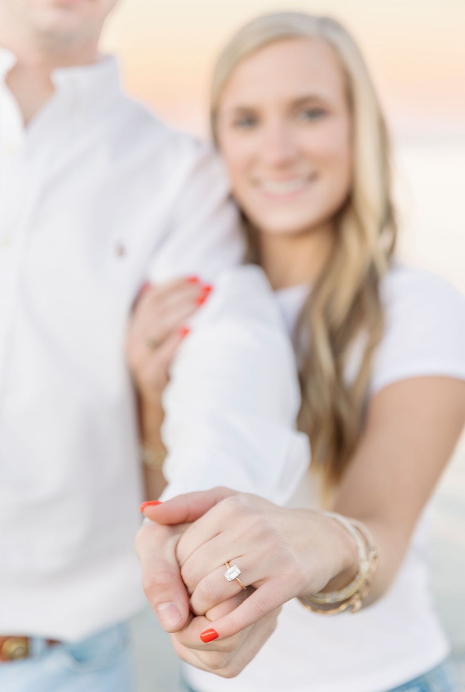 A couple shows off engagement ring with soft focus and warm lighting.