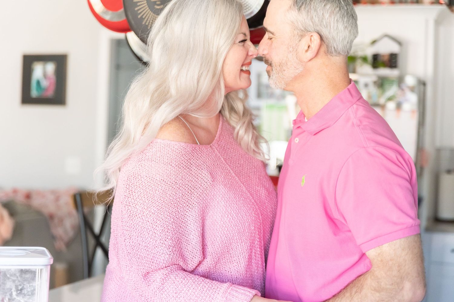 An intimate moment between a couple wearing matching pink outfits in their kitchen.