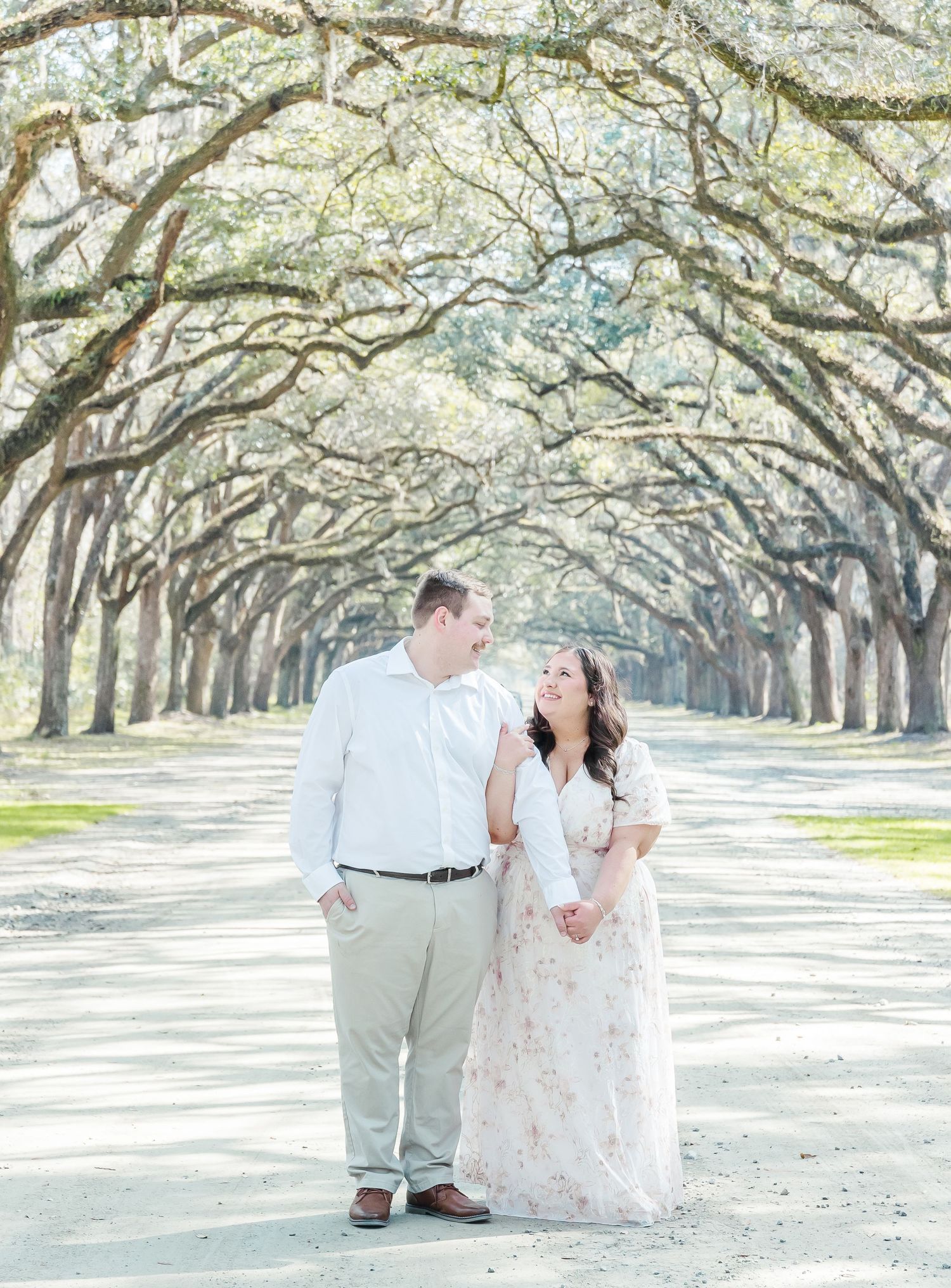 Couple sharing a romantic moment under an arched canopy of live oak trees.